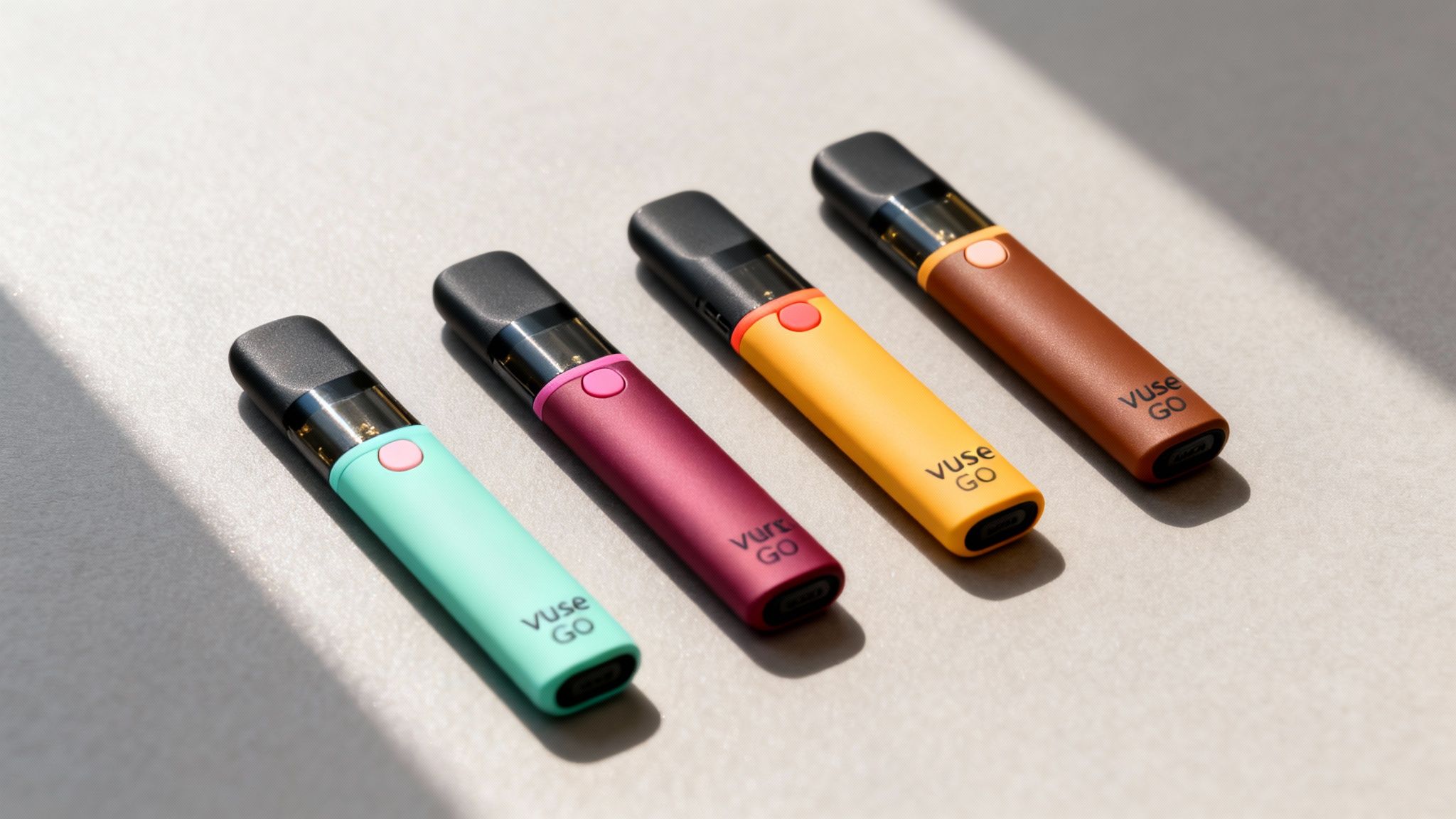 Four Vuse Go vaping devices in teal, magenta, yellow, and brown on a light surface.