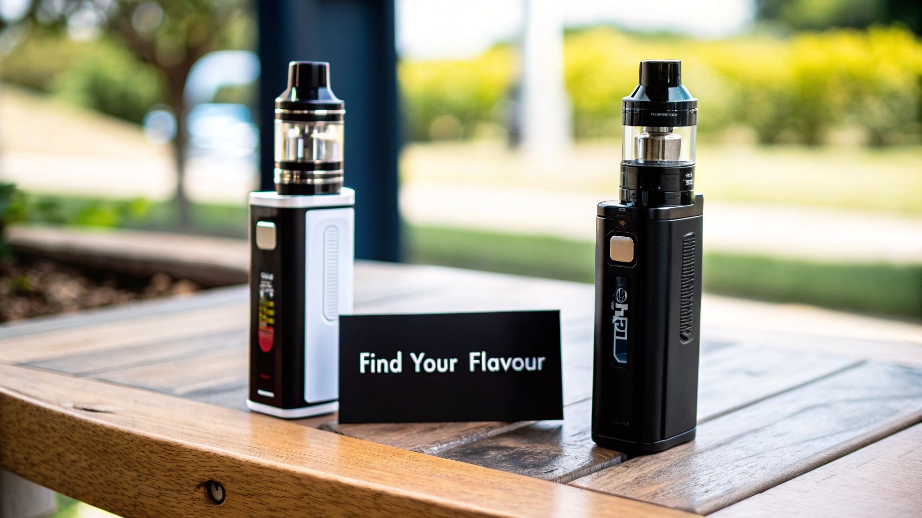 Two modern vape devices, one black and one black and white, sit on a wooden table next to a 'Find Your Flavour' sign.