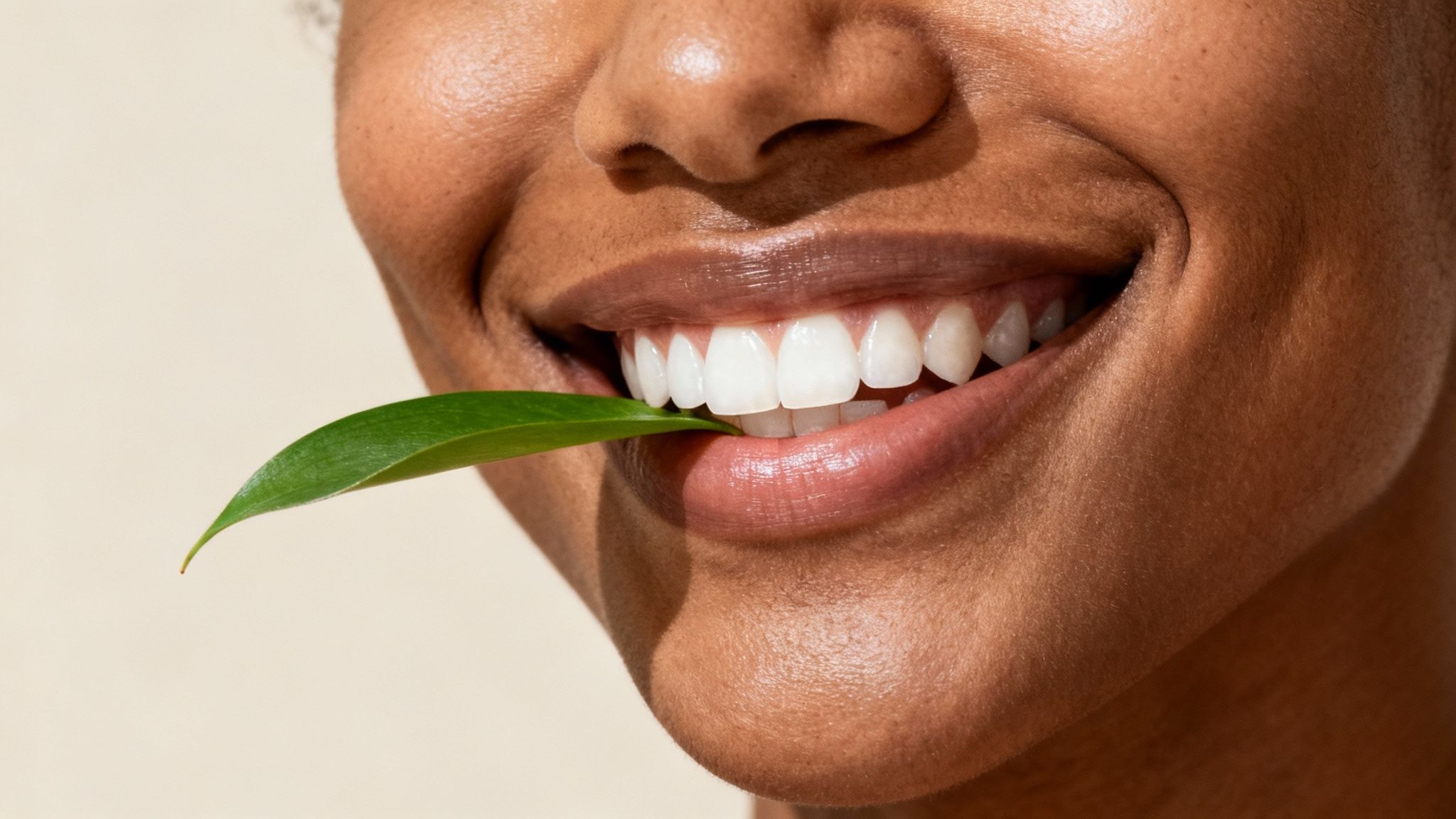 Smiling person with bright white teeth holding green aloe vera leaf between lips
