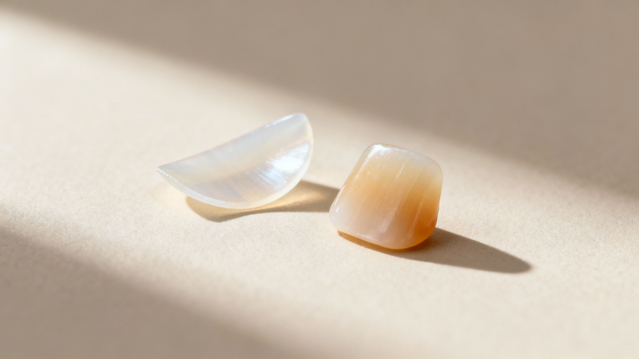 Close-up of two polished, translucent dental veneers, one white crescent and one peach rectangular.