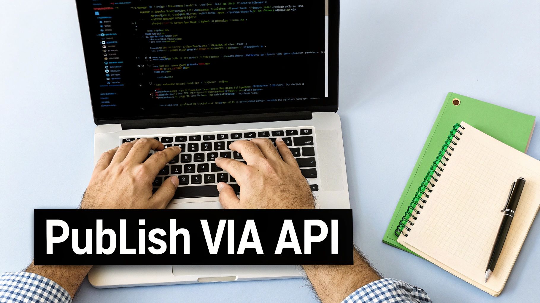 A person typing code on a laptop, with a notebook and pen, for publishing via API.