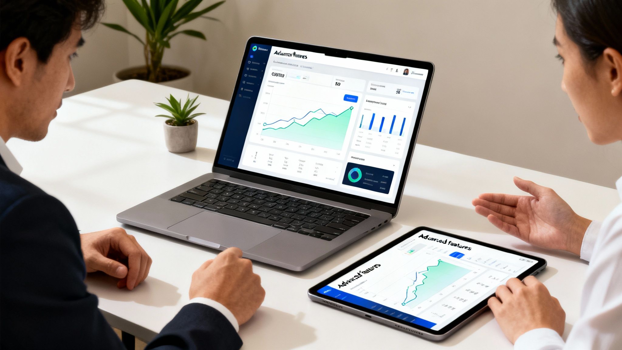 Two professionals discussing business data on a laptop and tablet in a modern office.