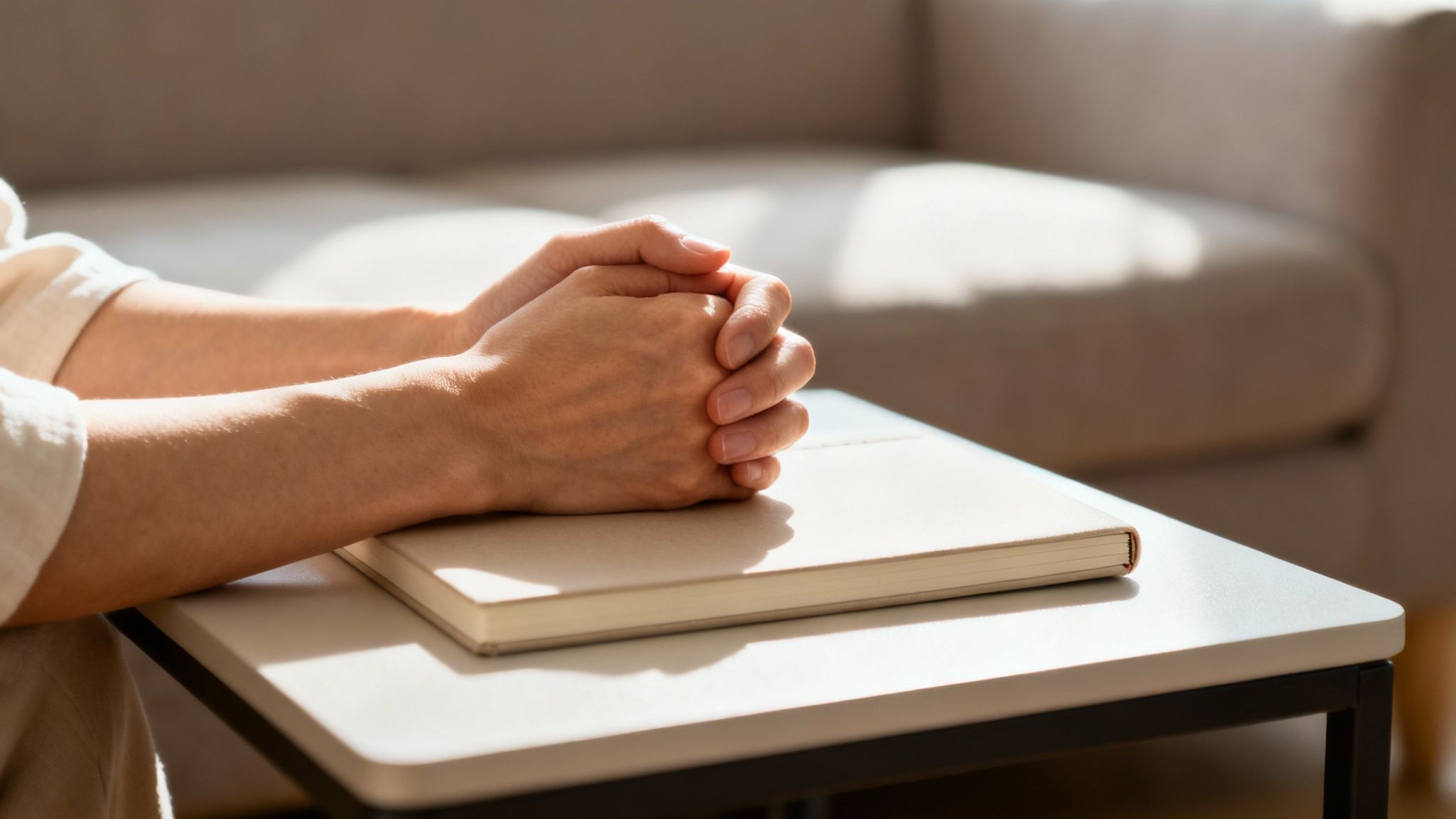 Close-up of a person's clasped hands resting on a notebook on a table, in a home setting.