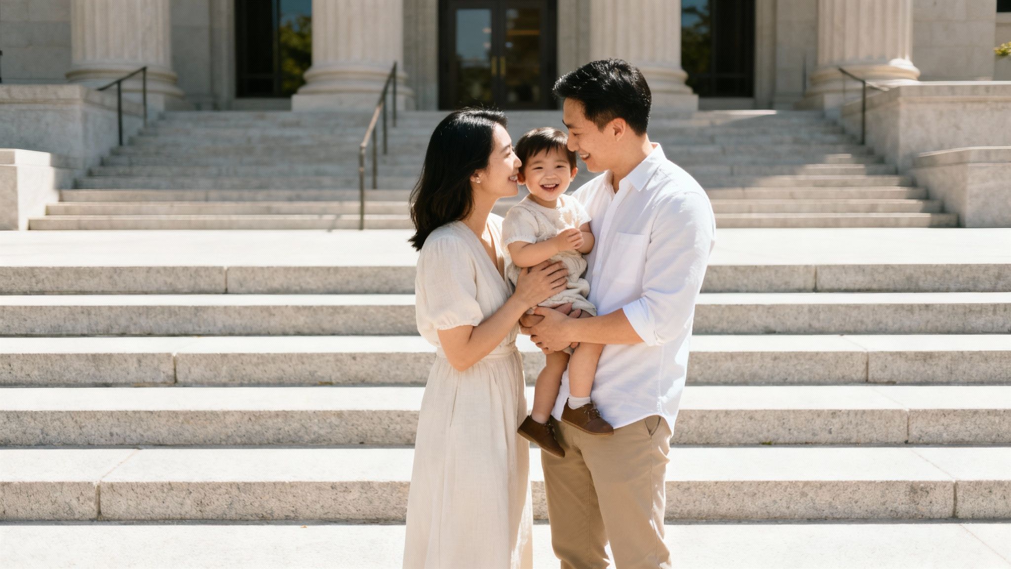 An Asian family with a smiling toddler stands in front of a grand building with stairs.