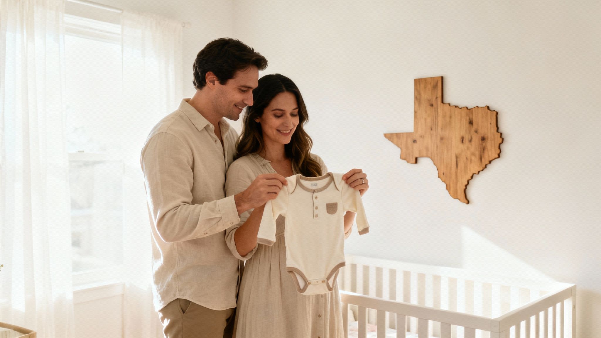 A happy couple smiles while holding a baby's onesie in a bright nursery with a Texas map.