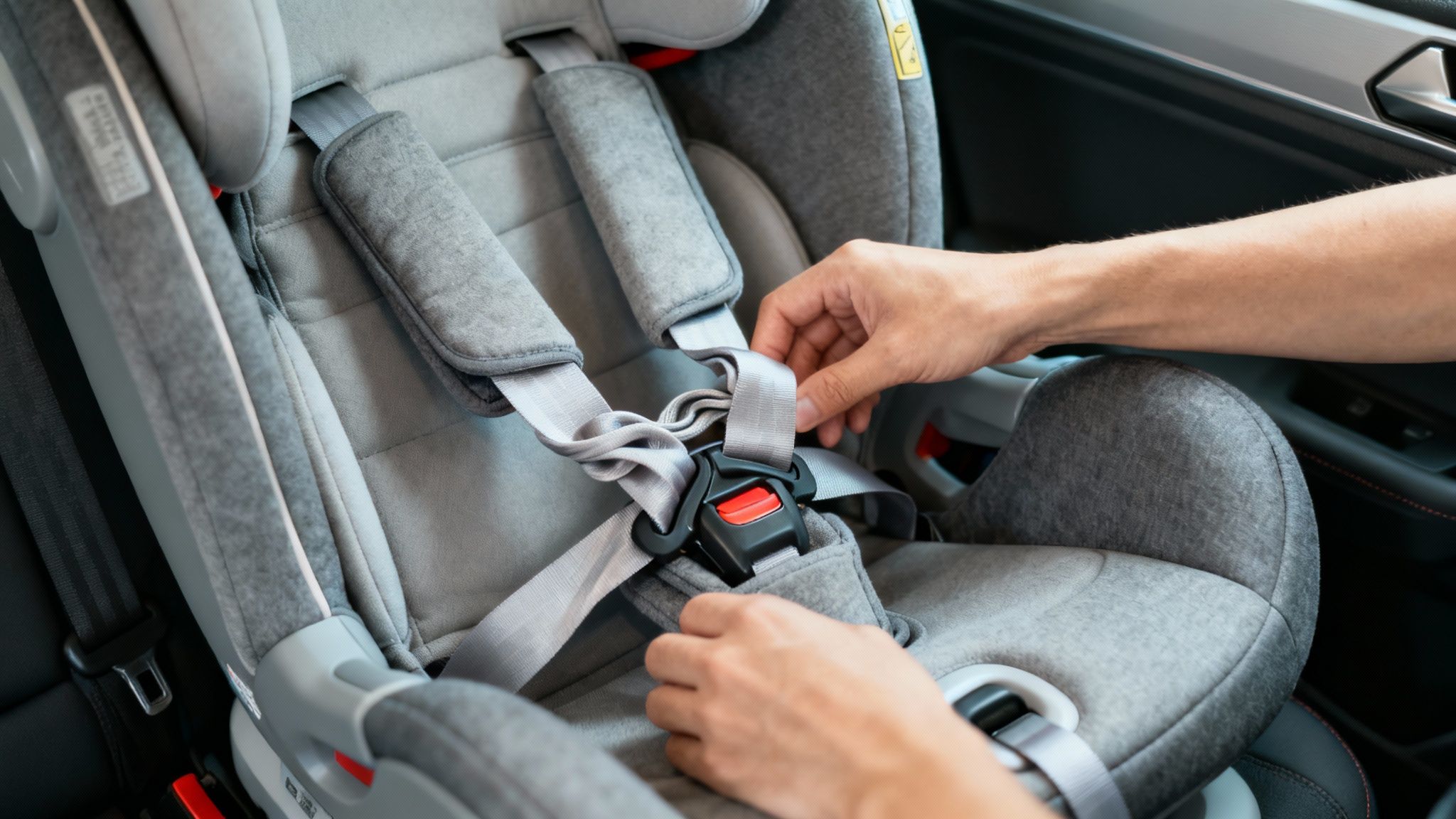 A parent carefully adjusts the straps on a child's car seat inside a vehicle.