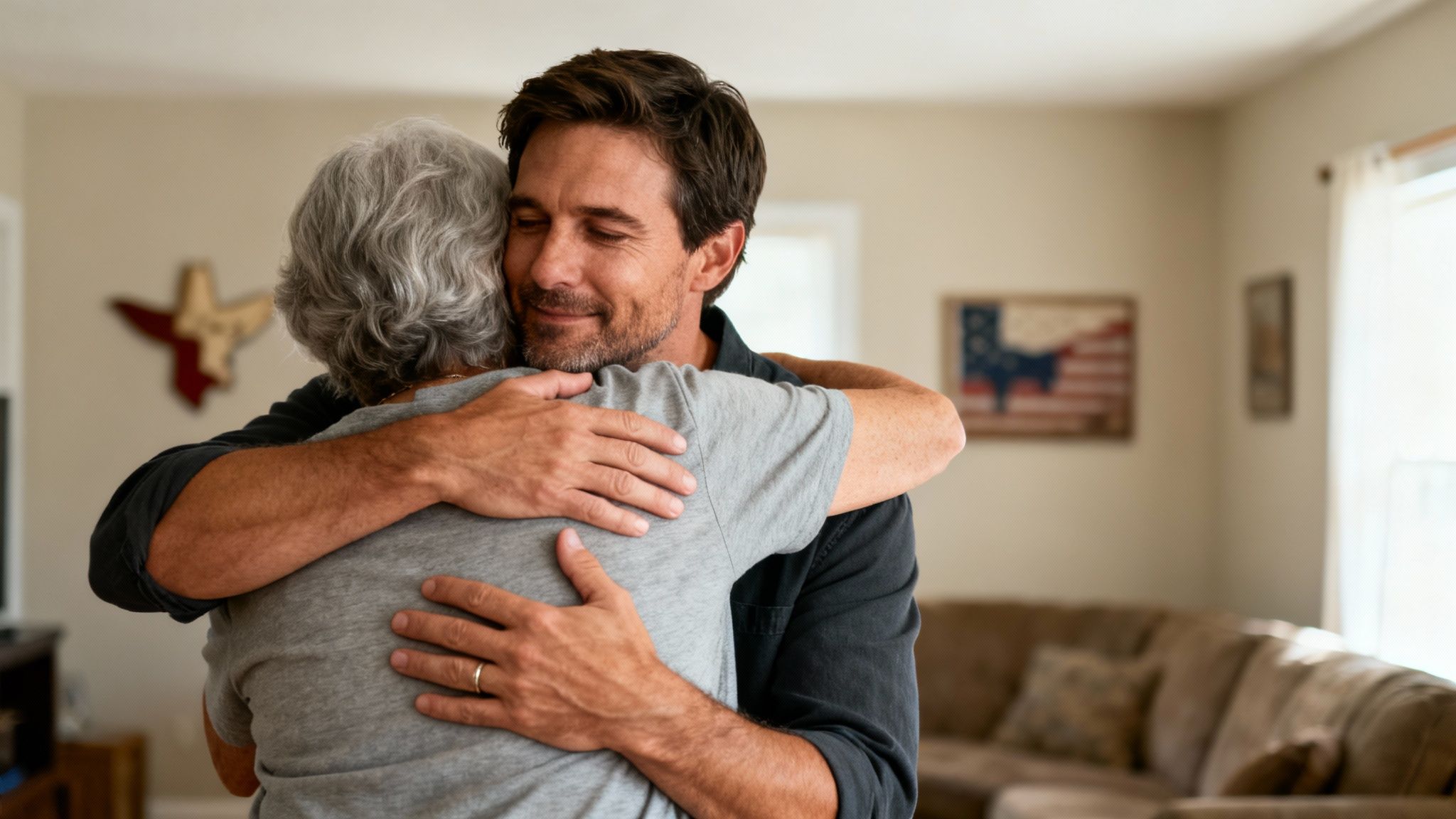 A loving man with closed eyes embraces an older woman with gray hair in a home setting.