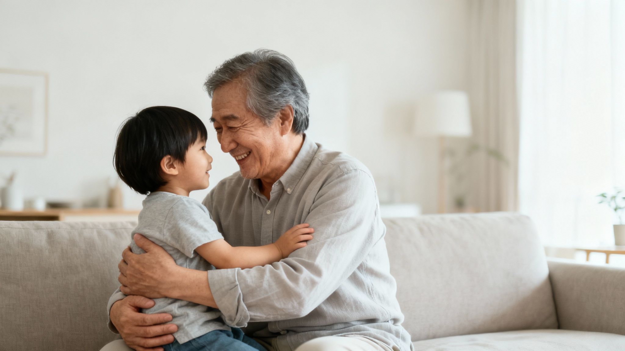 An elderly Asian man warmly hugs a young boy, both smiling and looking at each other.