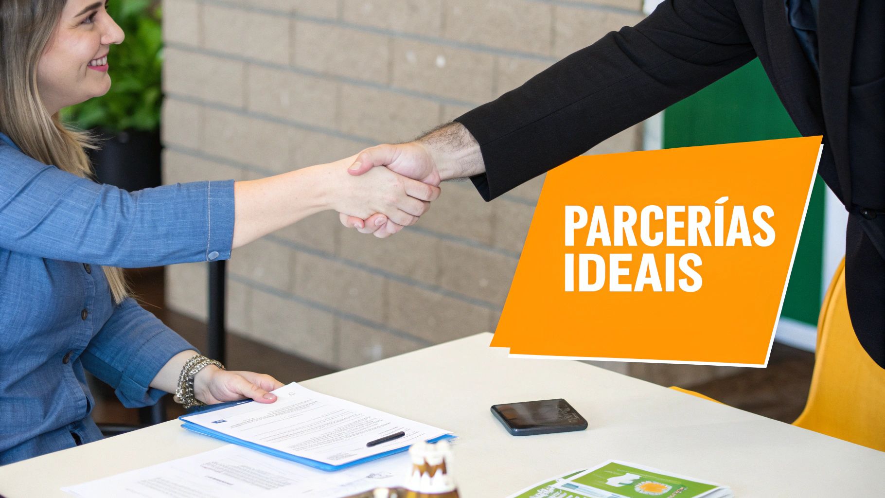 Duas pessoas apertam as mãos sobre uma mesa, simbolizando parceria, com documentos e um banner laranja "PARCERIAS IDEAIS".