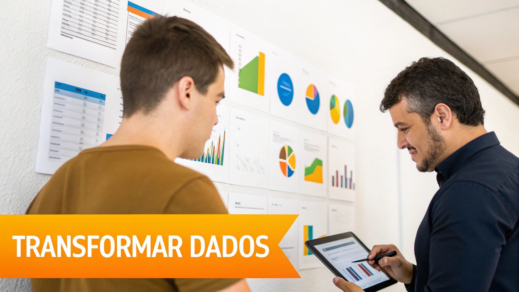 Dois homens analisando gráficos e dados em um painel na parede e tablet, com o texto 'TRANSFORMAR DADOS' em destaque.