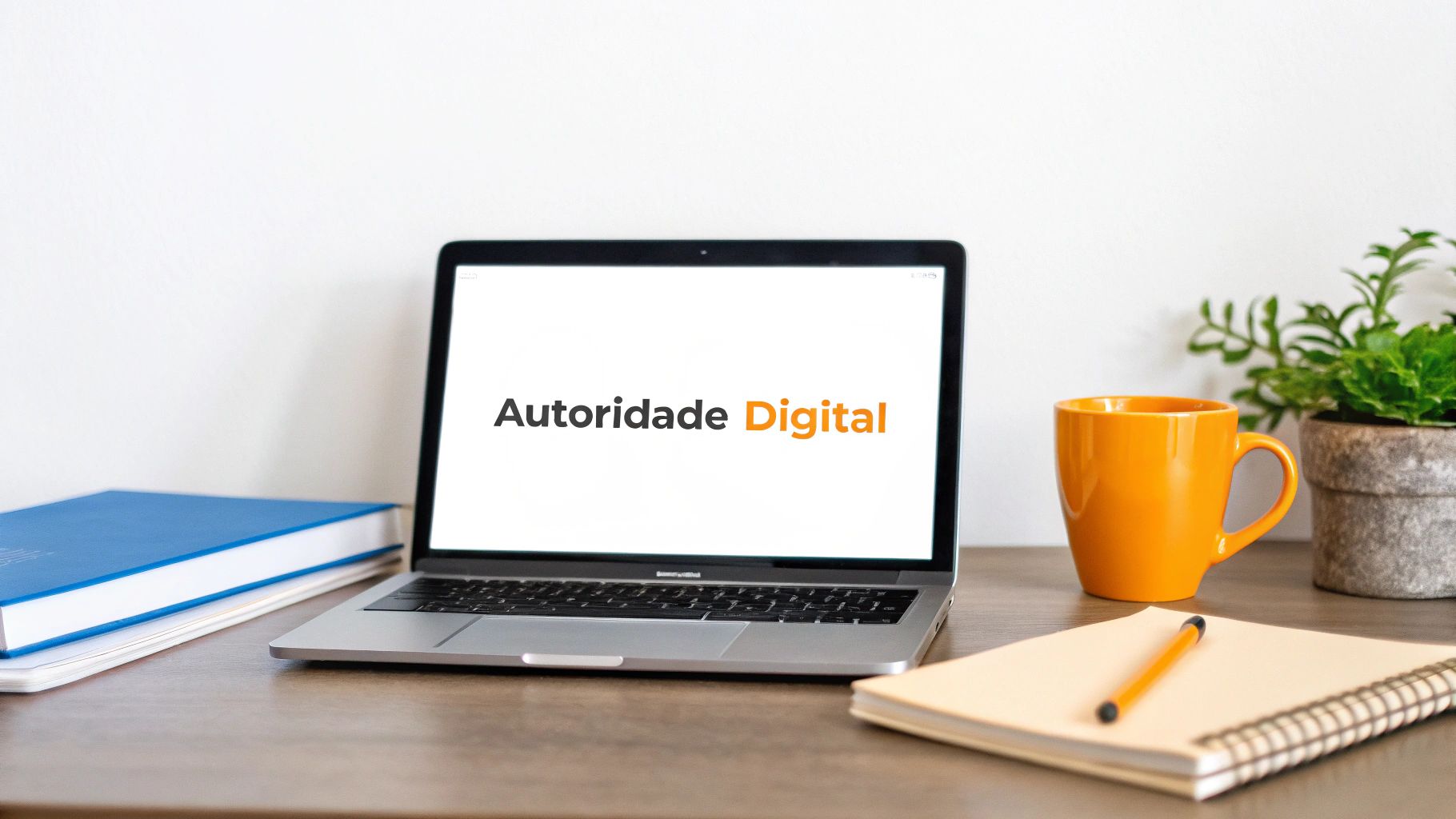 Laptop na mesa de madeira com 'Autoridade Digital' na tela, cercado por livros, caneca e planta.