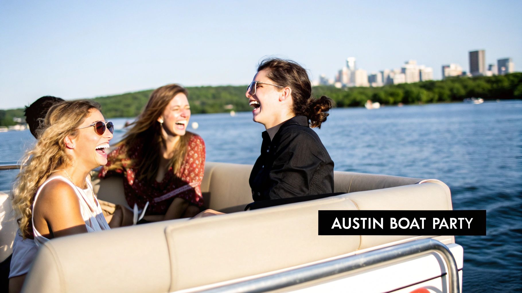 Three happy young women laughing and enjoying a boat party on a sunny day with a city skyline in the background.