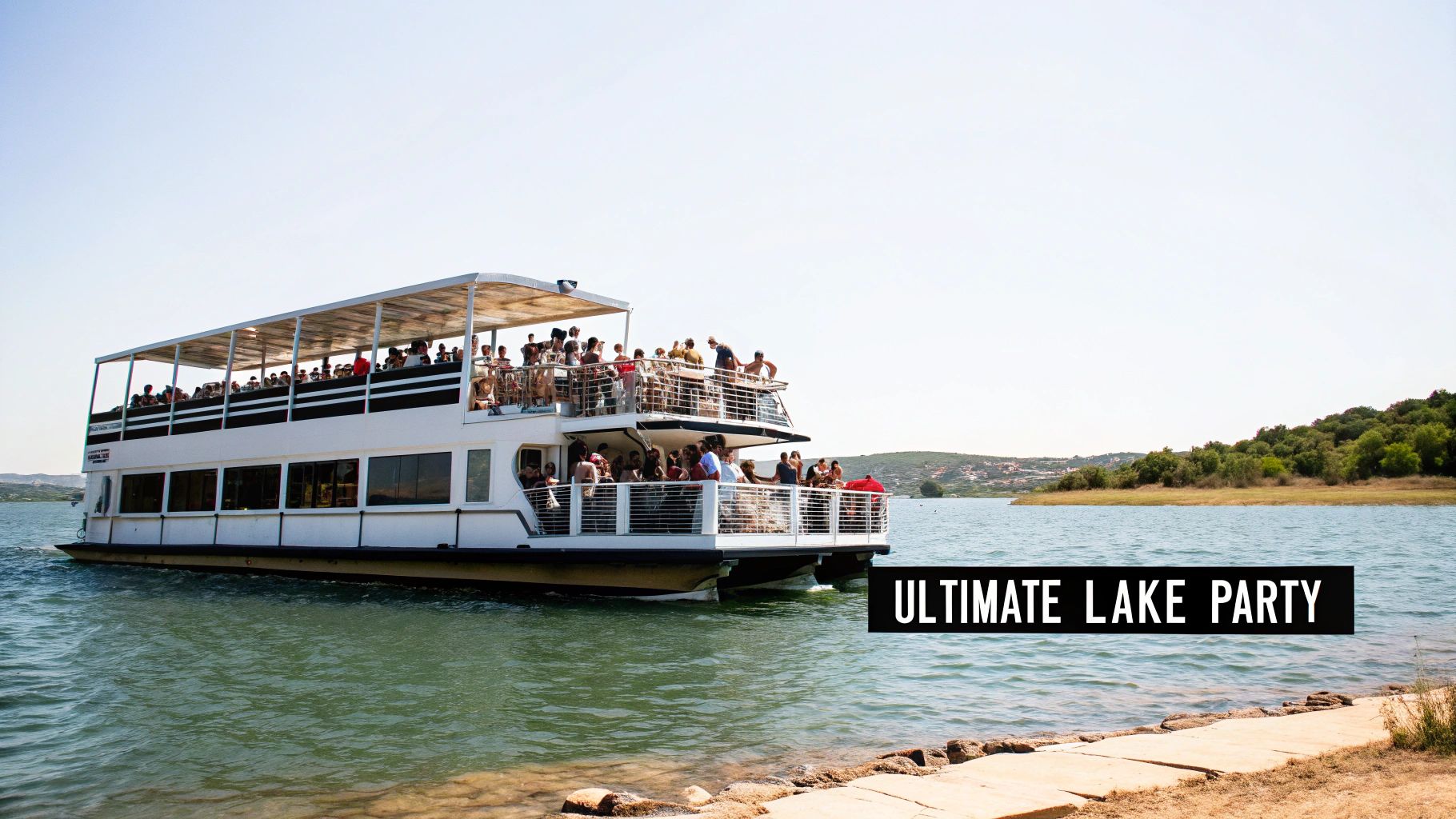 A large two-deck party boat full of people cruises on a lake under a clear sky.
