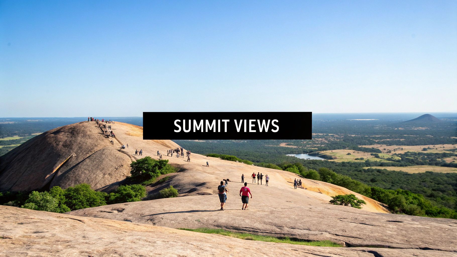 Hikers ascend a vast granite dome, offering panoramic views of a lush landscape with a lake.