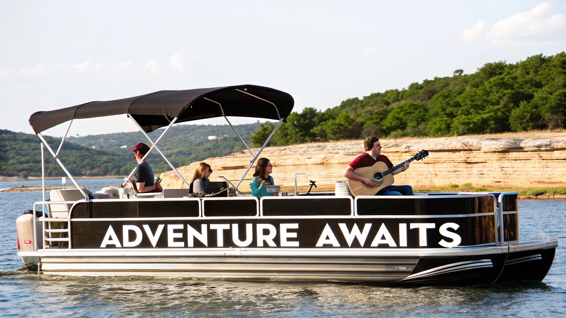 People enjoy a sunny day on a pontoon boat with 'ADVENTURE AWAITS' on its side, a man plays guitar.