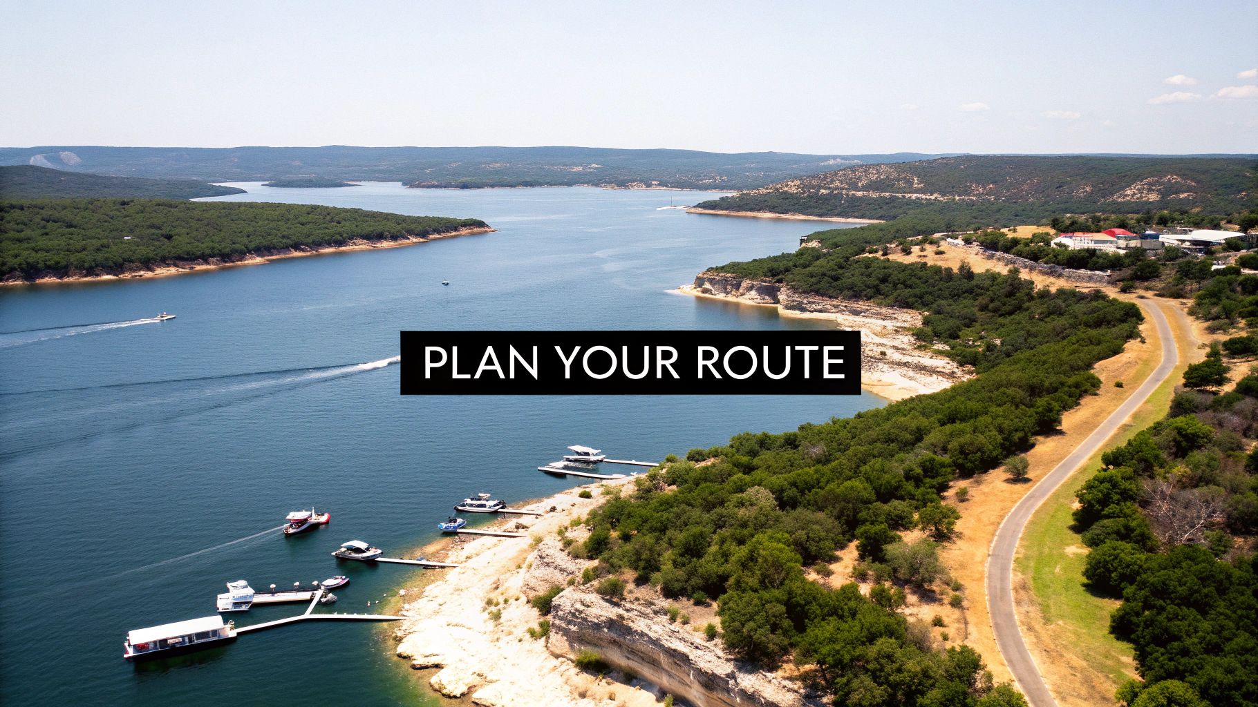 Aerial view of a scenic lake with boats, green shores, a winding road, and 'PLAN YOUR ROUTE' text.
