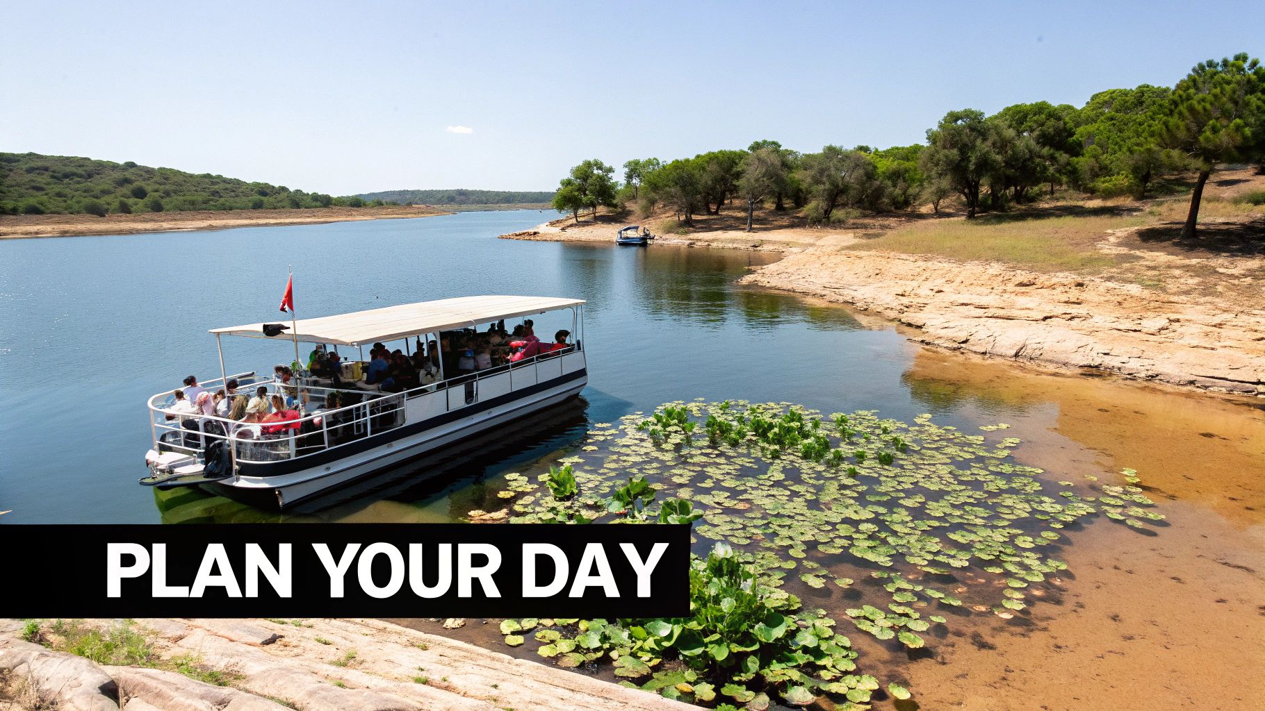 A large tour boat full of people cruises on a sunny lake surrounded by green trees and rocky shores.