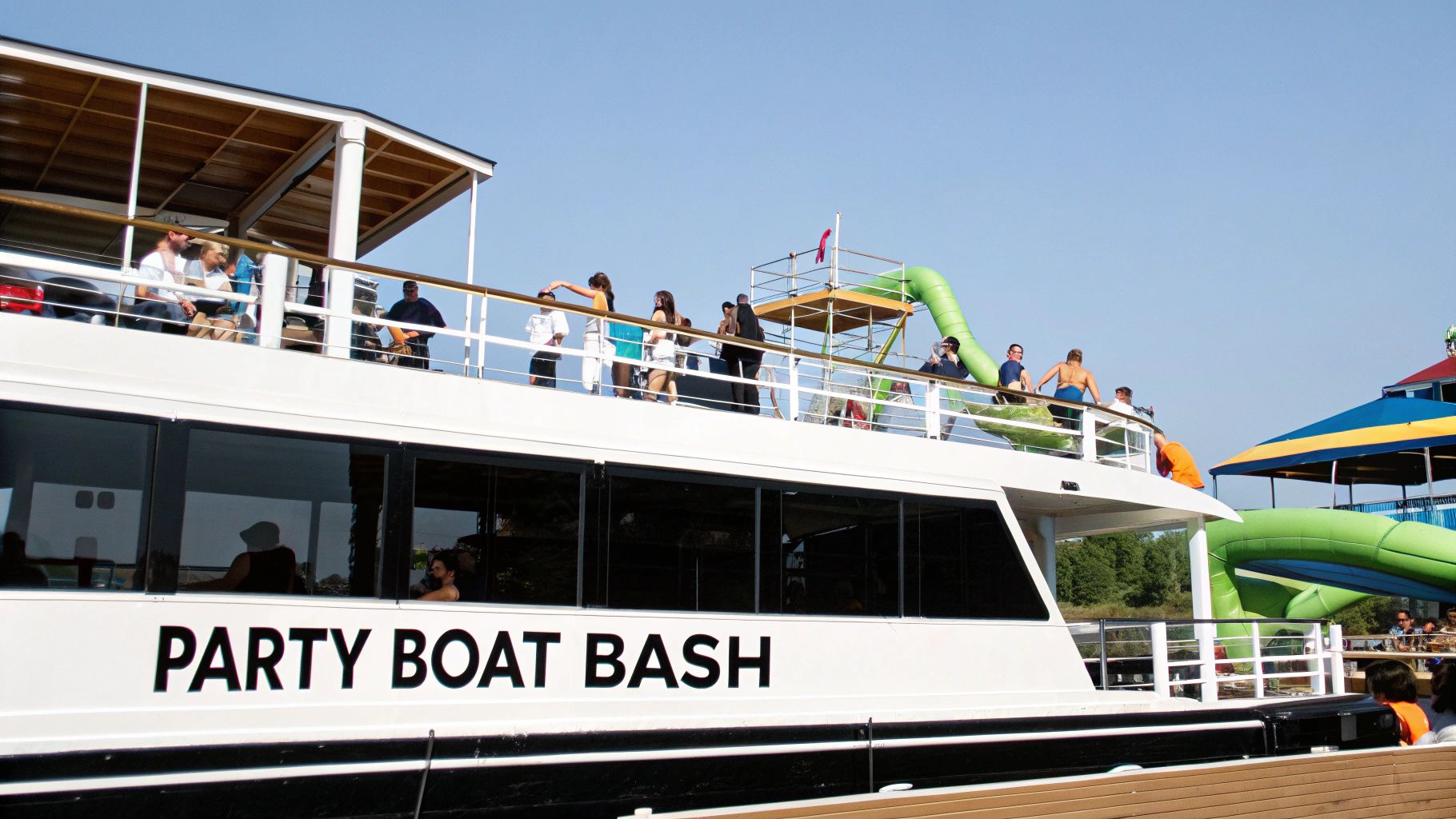 People enjoying a party boat with a large green inflatable slide under a clear sky.