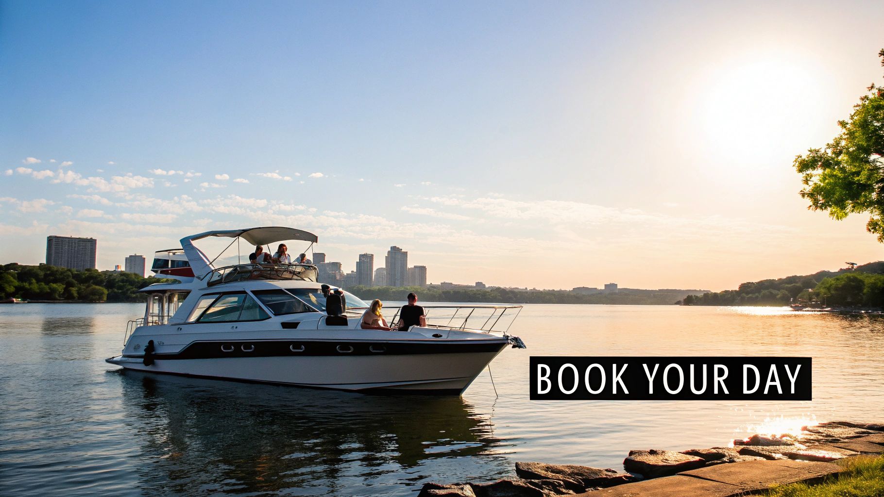 A white yacht with people enjoying a leisurely cruise on a lake during a golden sunset, with a city skyline in the background.