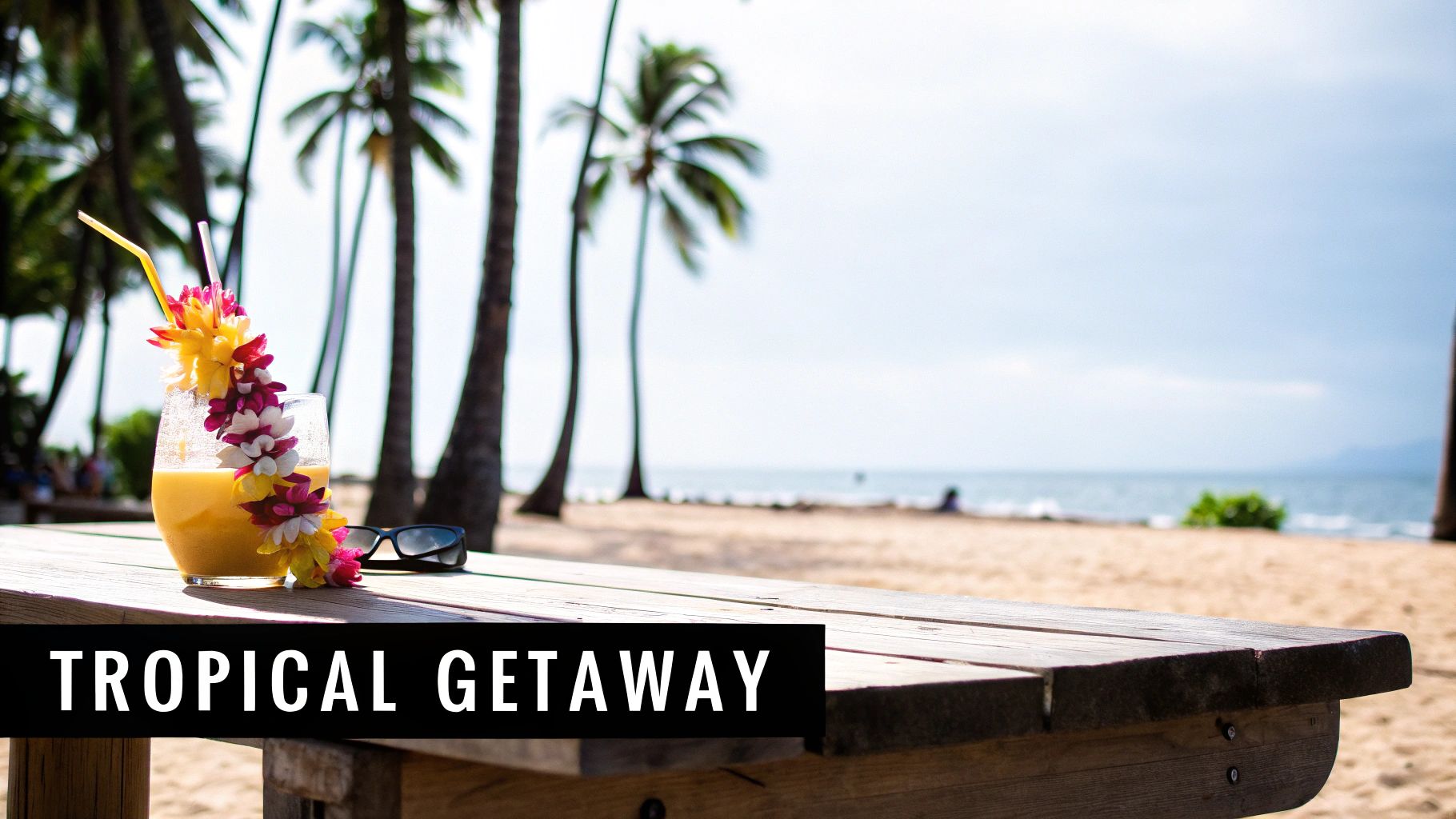 A tropical drink with a flower lei and sunglasses on a wooden table at a sunny beach.