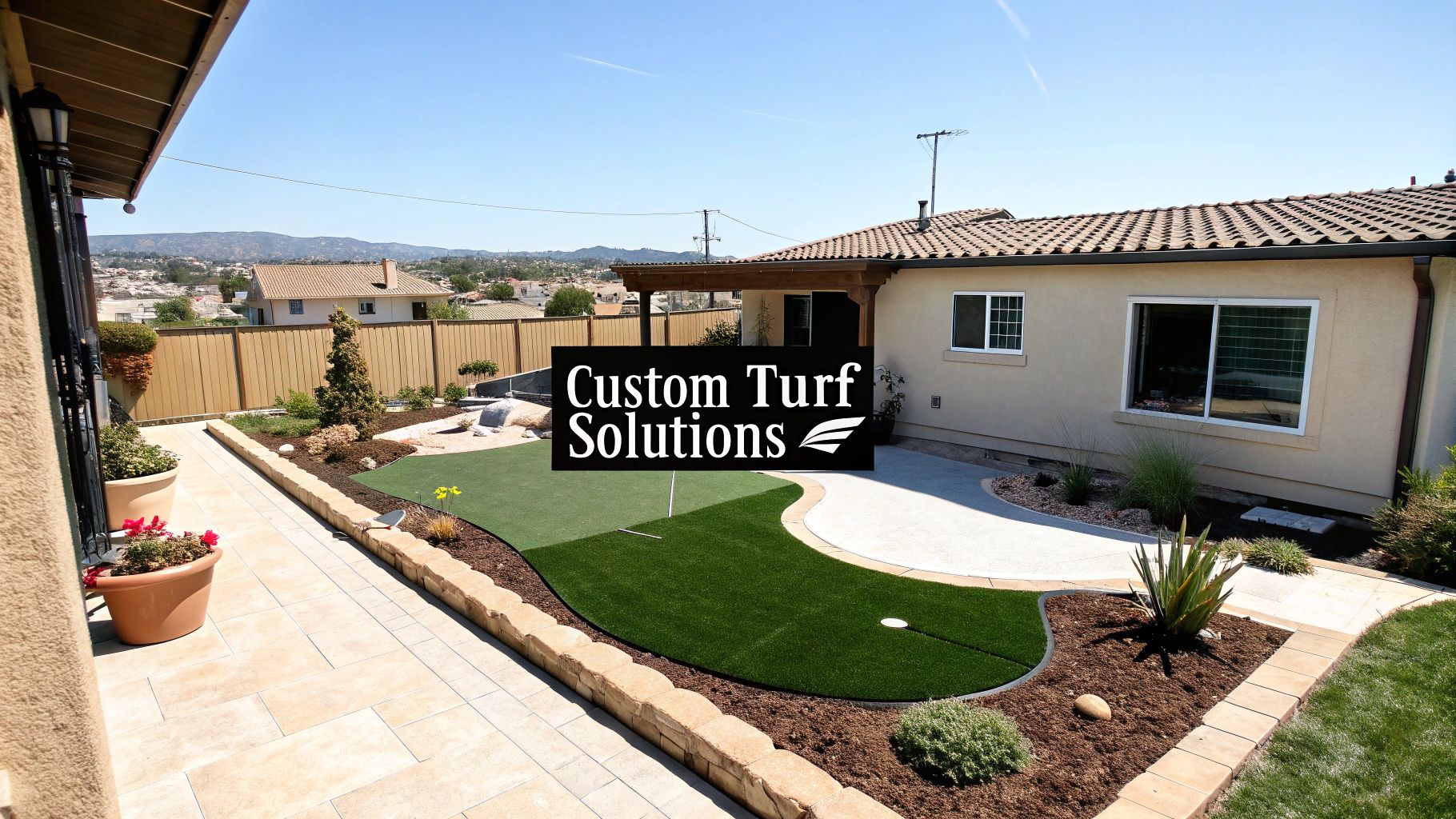 A custom backyard features an artificial turf putting green, a paved patio, and landscaped areas next to a house.