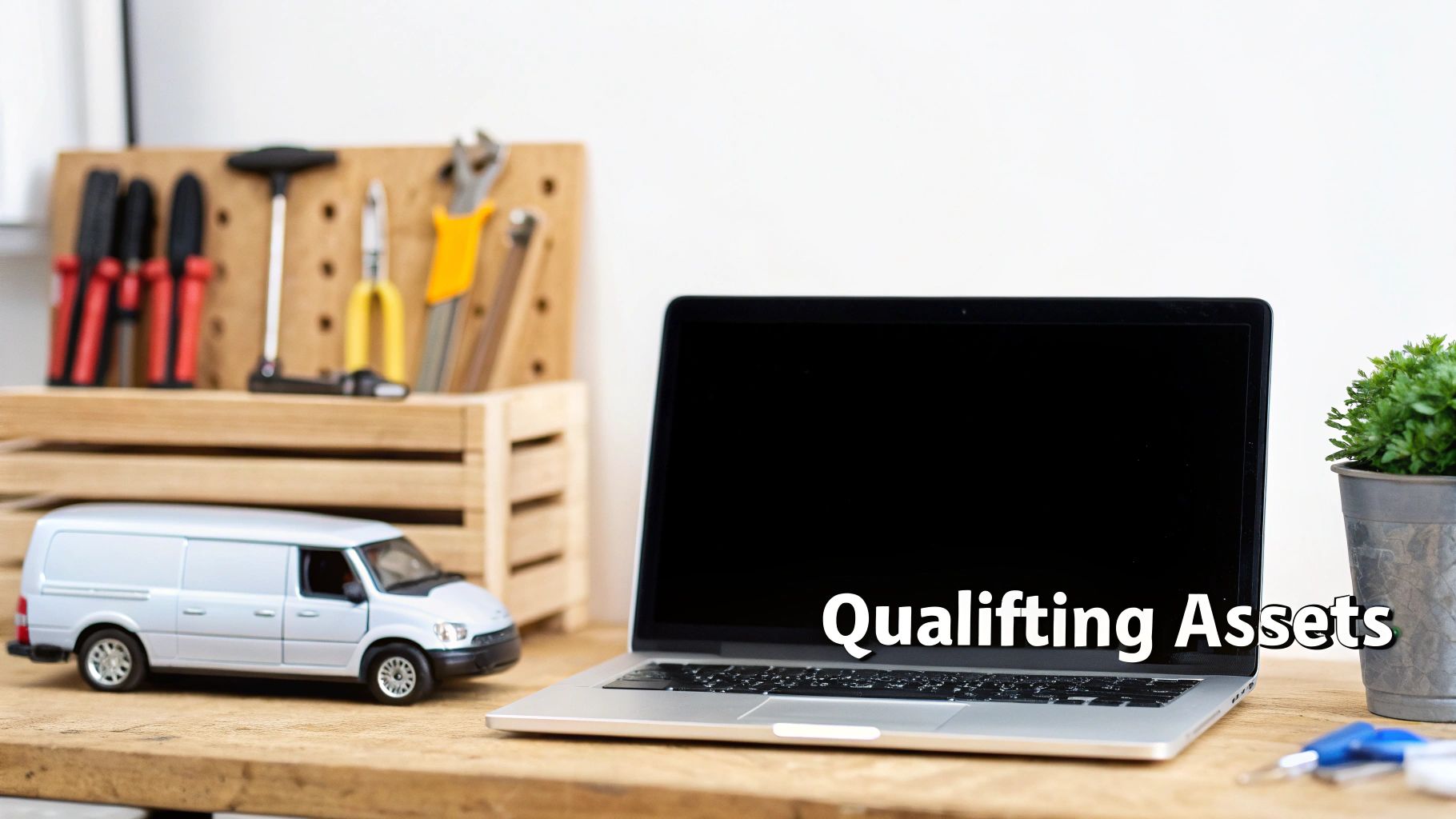 A desk with a laptop displaying 'Qualifying Assets', a model delivery van, and various tools.