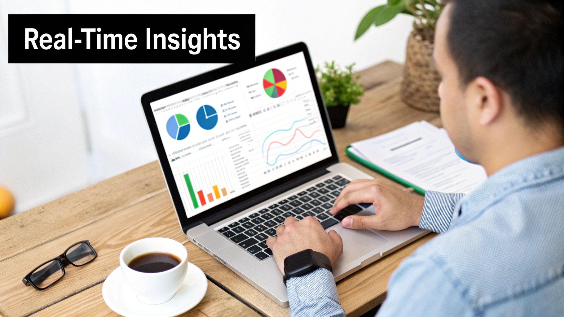 A person works on a laptop showing real-time data insights, charts, and graphs on a wooden desk.