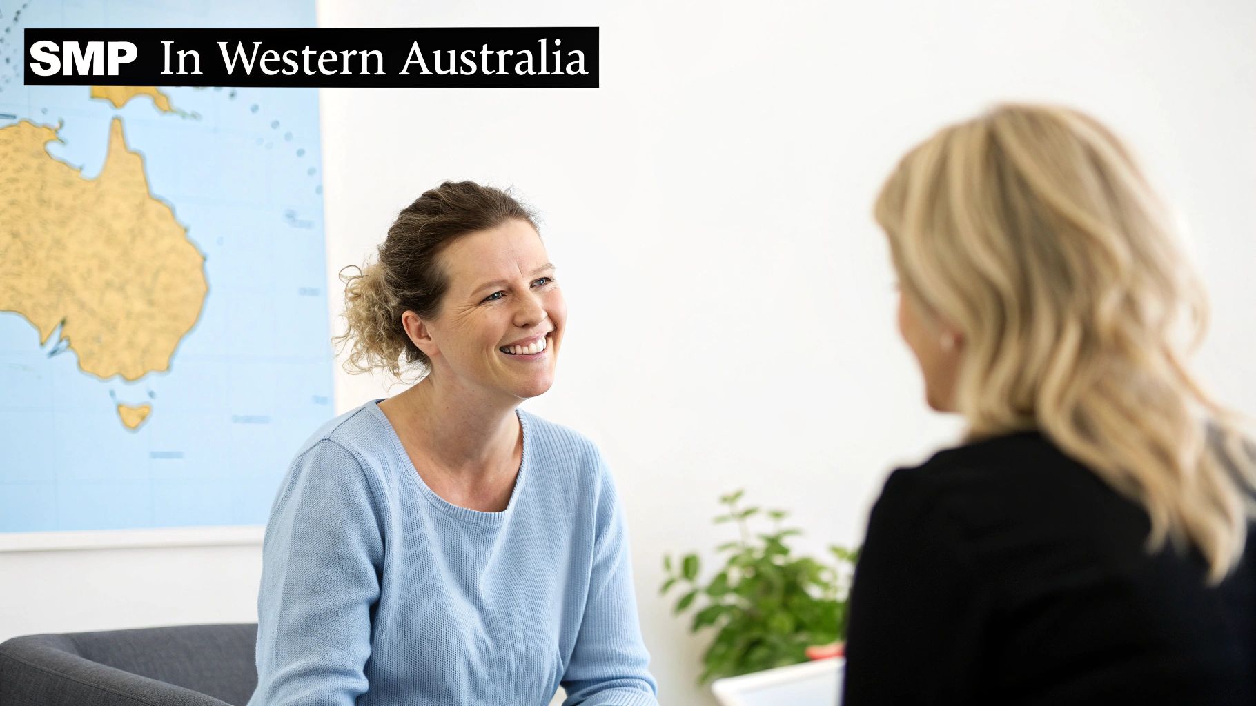 A smiling woman in a blue top talks with another person, with a map of Australia in the background.