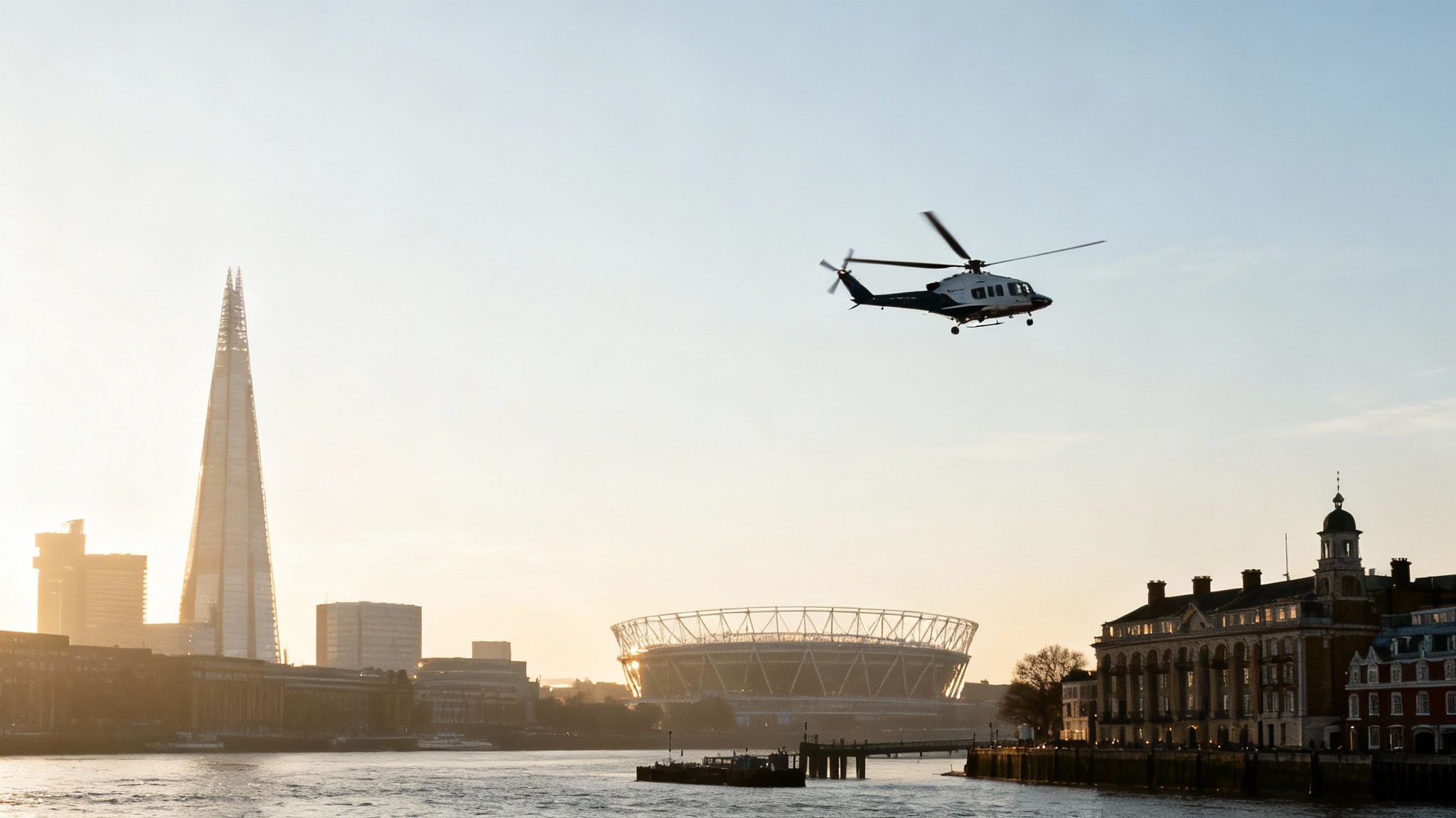 A helicopter flies over London's River Thames, featuring The Shard, a stadium, and buildings at sunset.