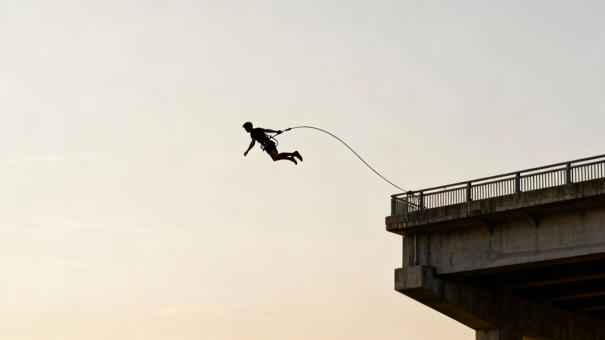 A thrilling silhouette of a person mid-air during a bungee jump from a concrete bridge.