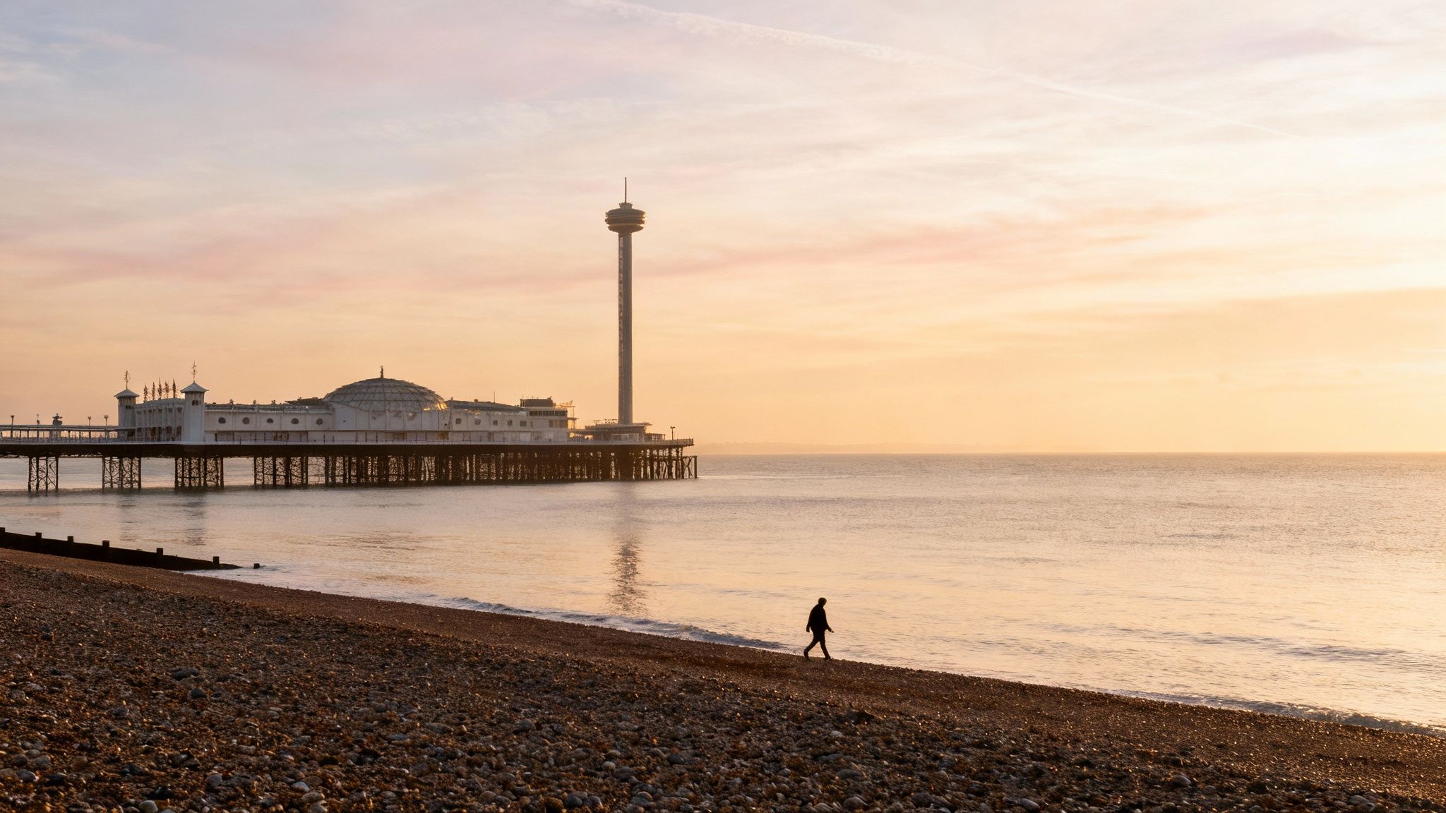 Sunrise over Brighton beach with Palace Pier, i360 tower, and a lone walker.