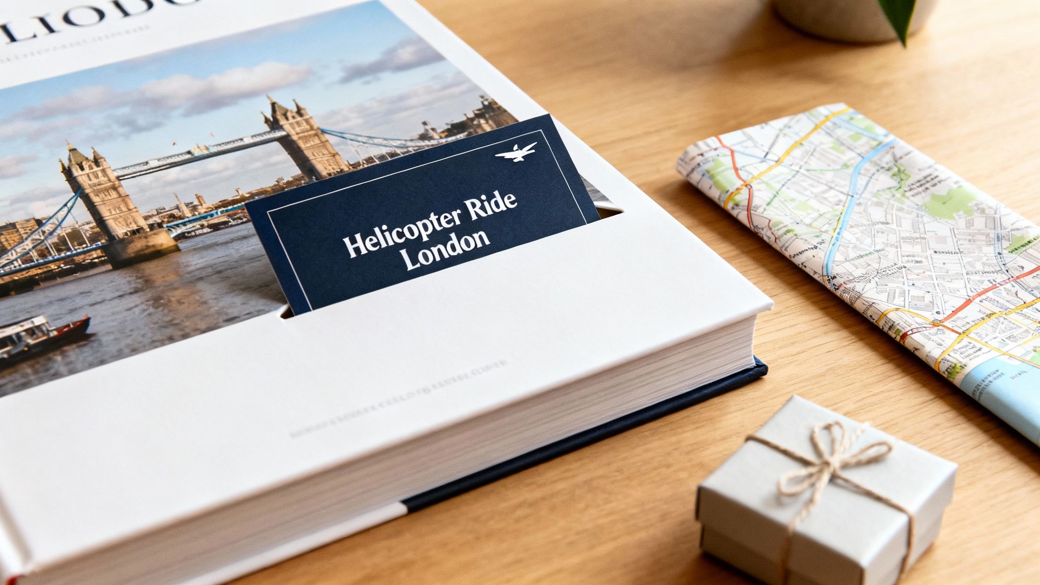 A book open to a page featuring Tower Bridge, with a 'Helicopter Ride London' bookmark, alongside a folded map and a small gift on a wooden table.
