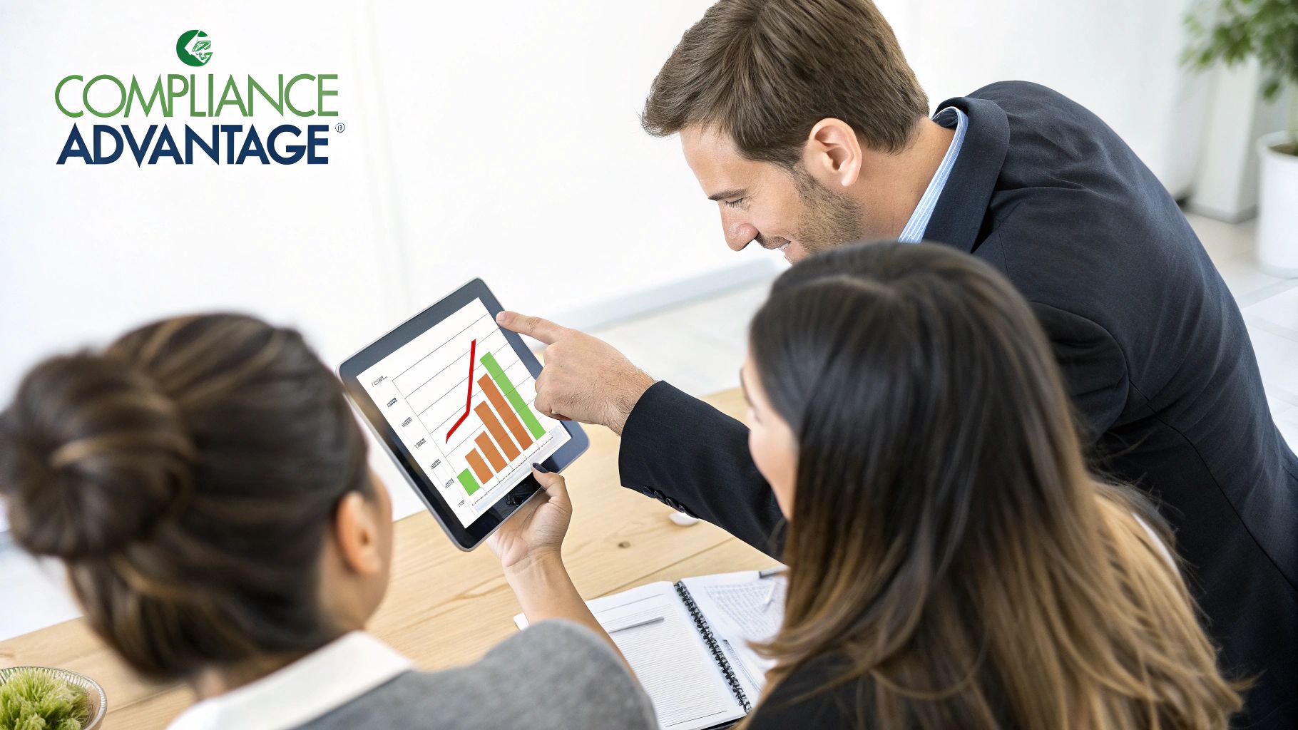 Business professionals discuss compliance data on a tablet, analyzing graphs during a meeting.