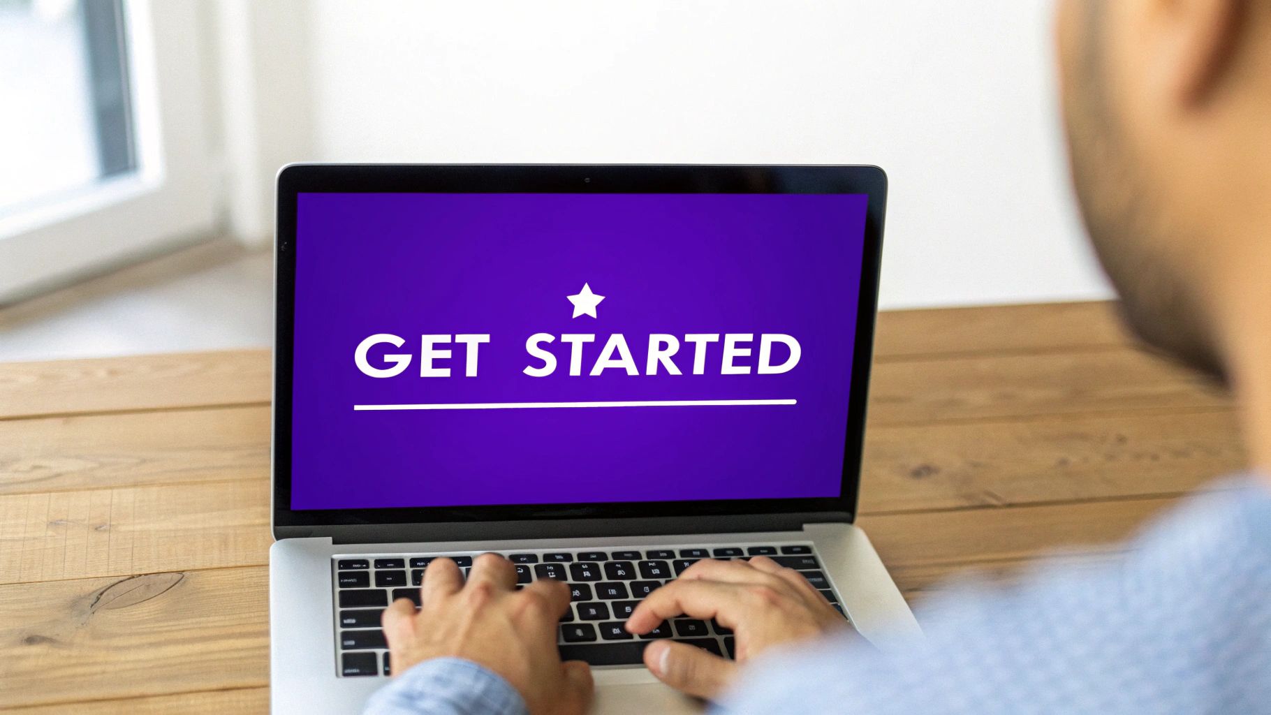 A person typing on a laptop displaying a purple screen with 'GET STARTED' text and a star icon.