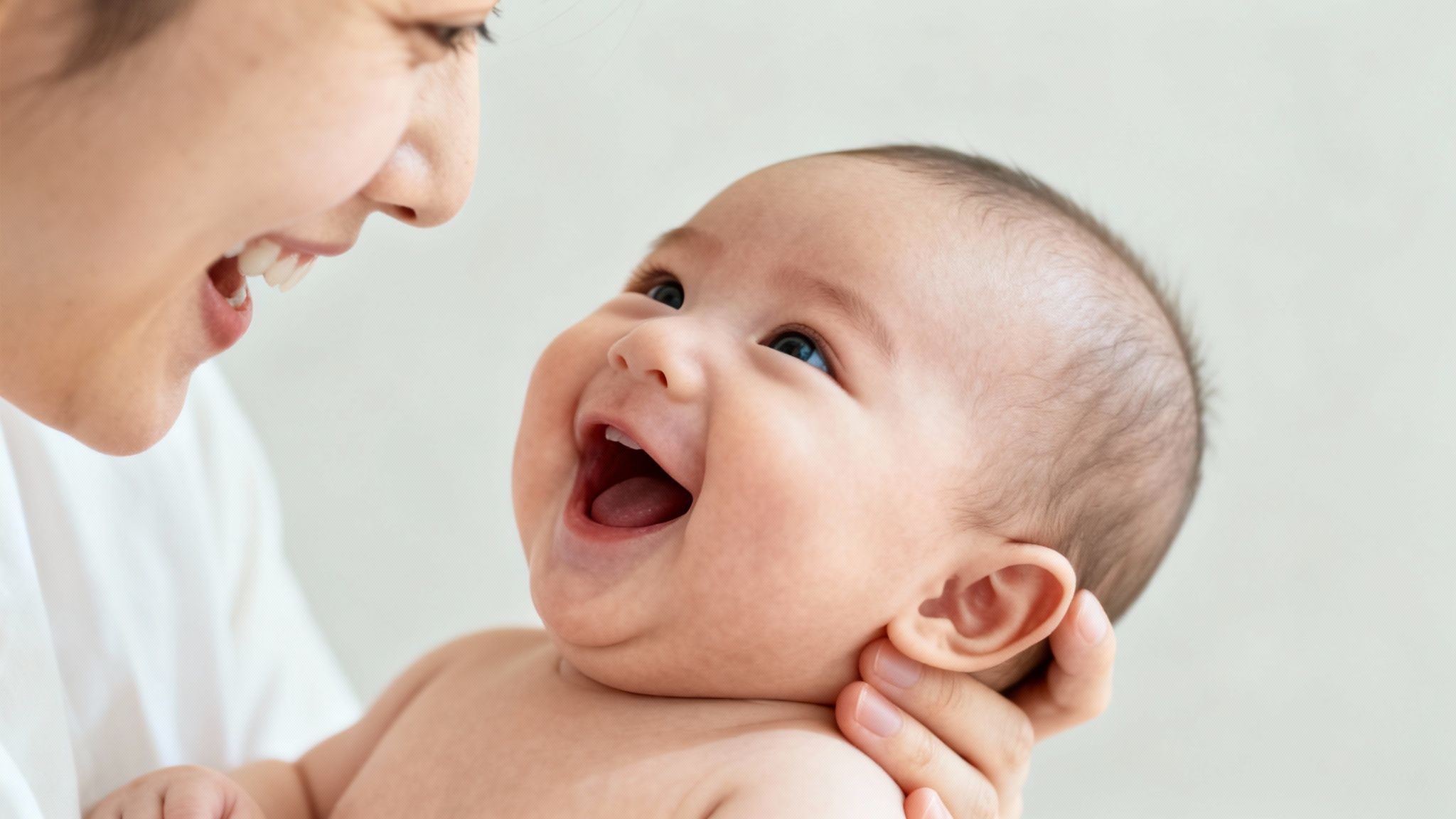 Joyful close-up of a smiling mother looking at her laughing baby held in her arms.