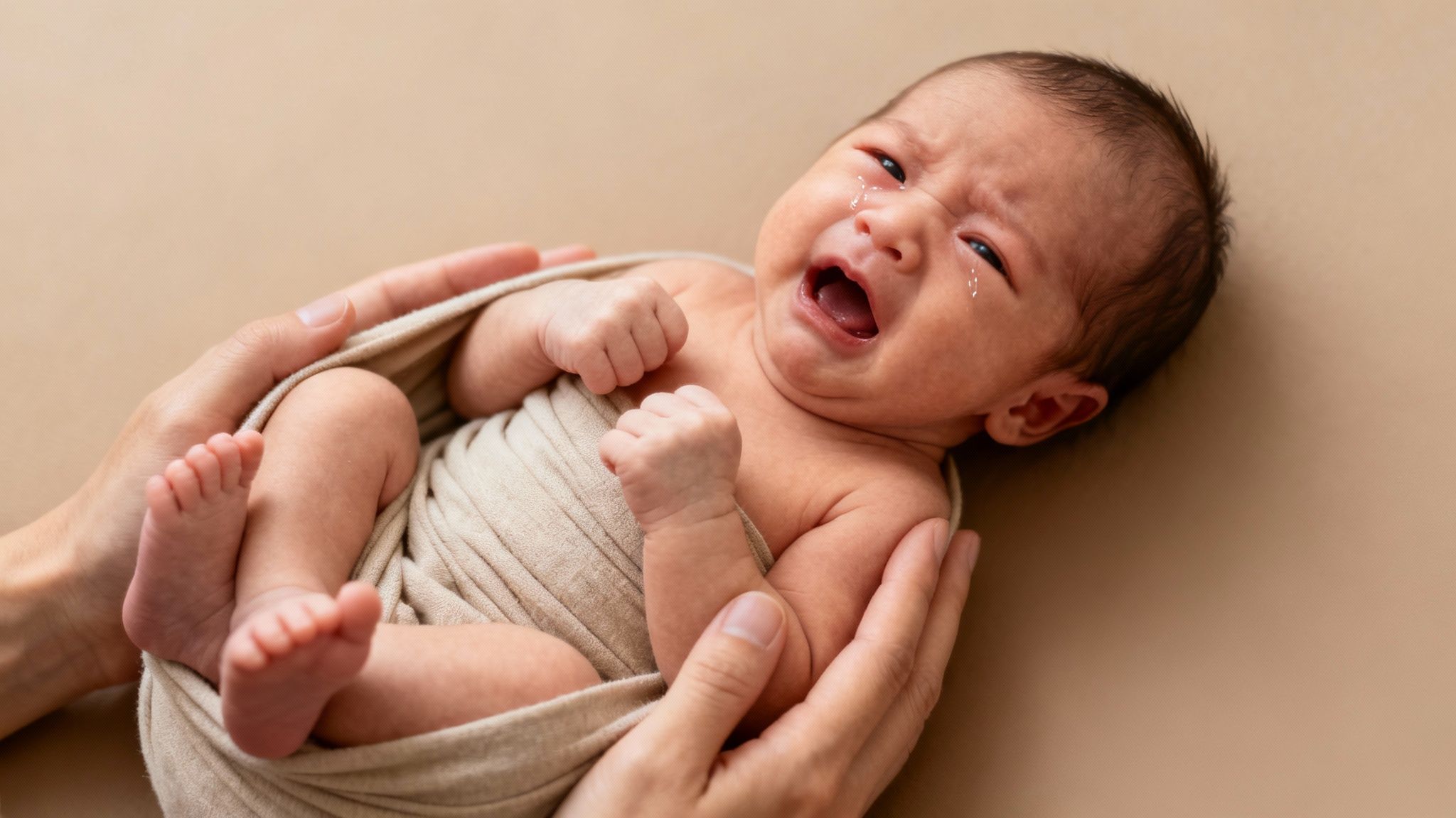 A mother holds her fussy newborn baby in a softly lit room.