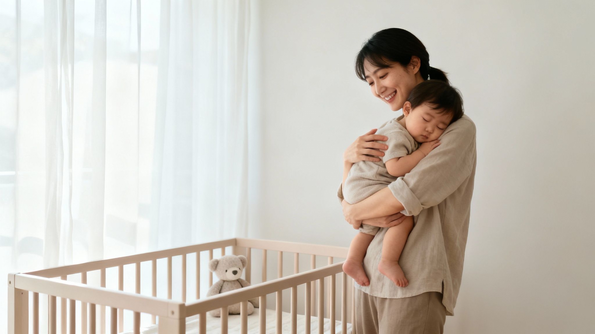 A happy mother gently holds her sleeping baby close, next to a crib with a teddy bear.