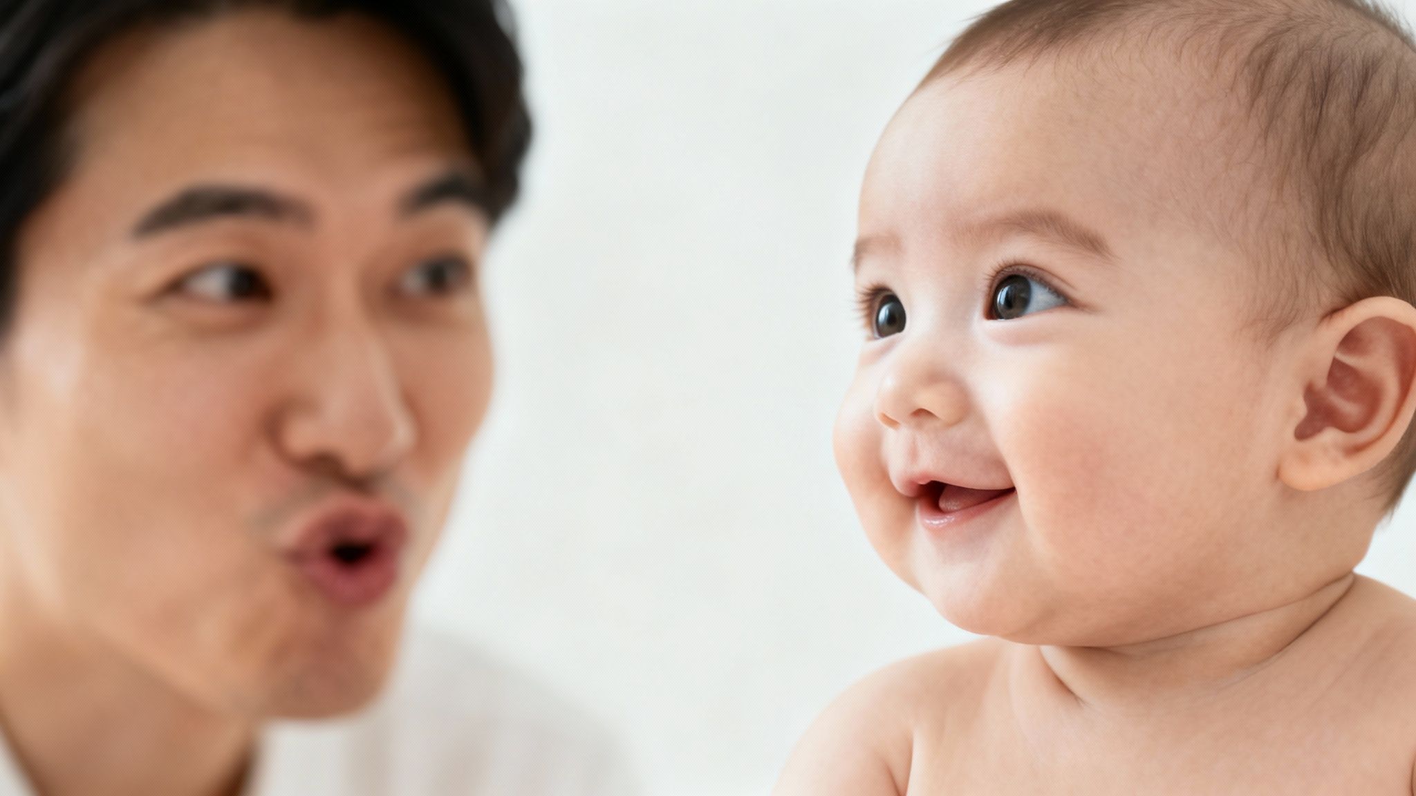 A cute baby with an open mouth smiles broadly at a father making a funny face.