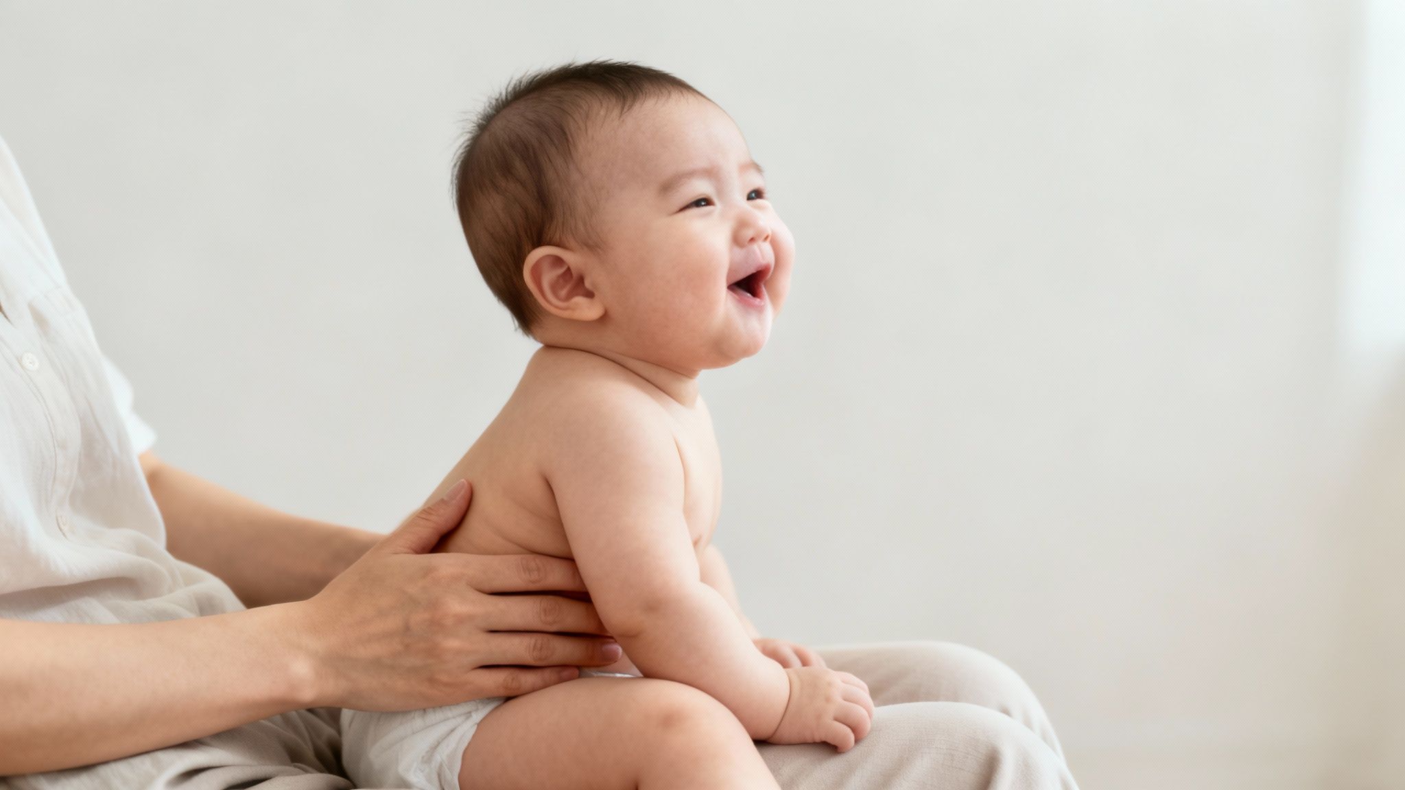 An adorable baby smiling brightly while being gently held on a parent's lap.