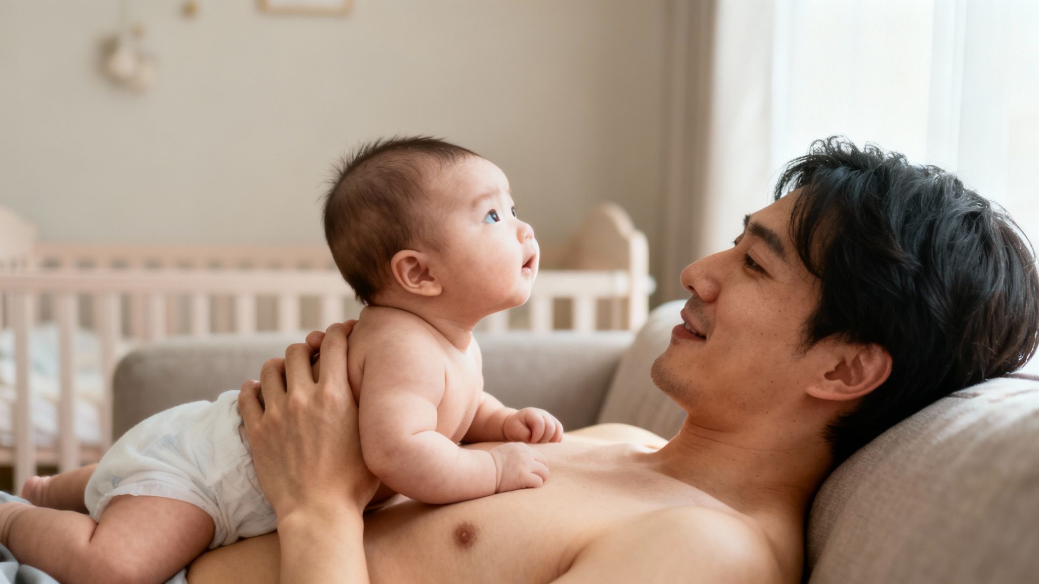 A father lies on a couch, gently holding his baby on his chest during tummy time.