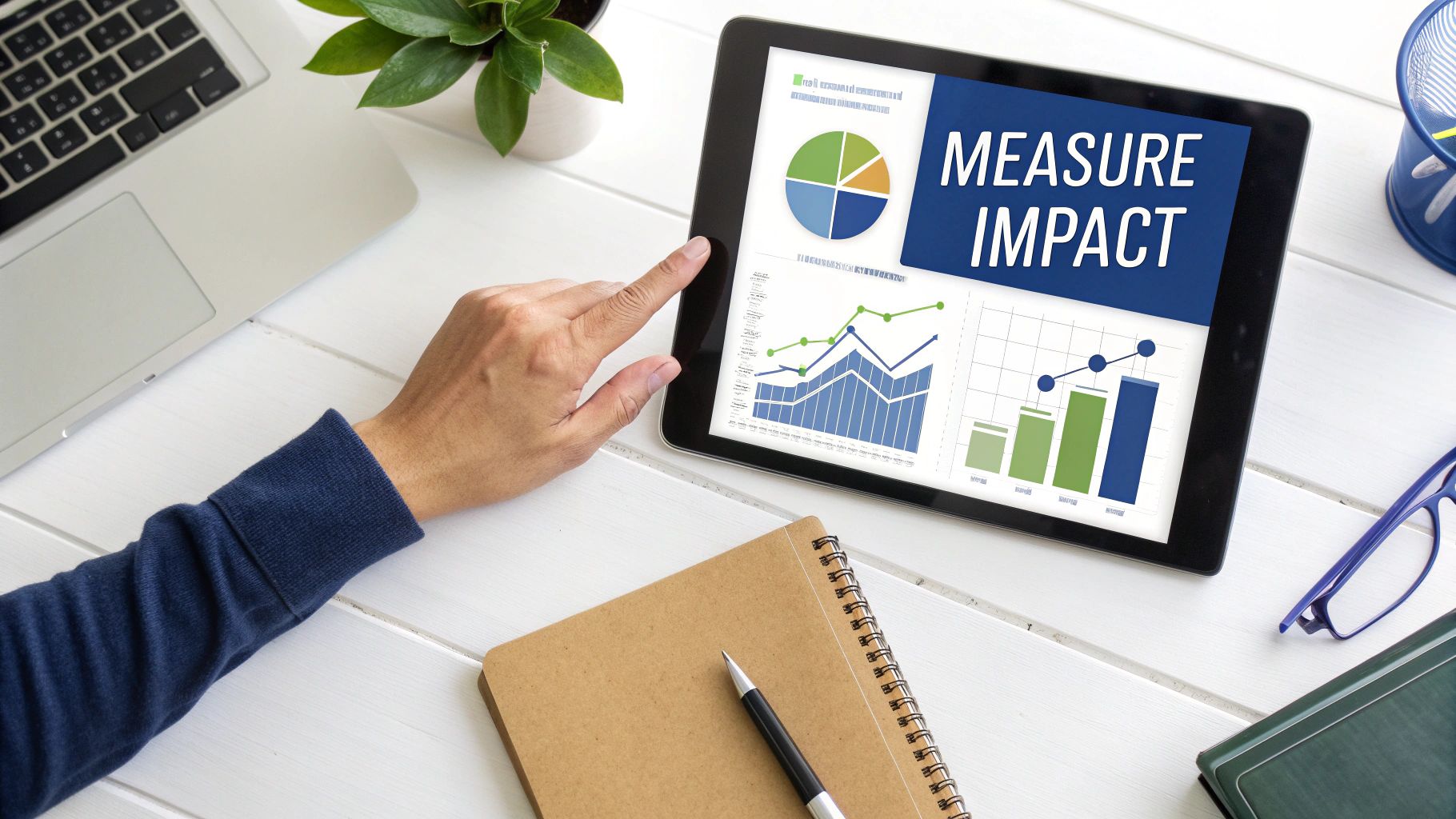 Overhead view of a person using a tablet displaying business charts and 'MEASURE IMPACT' text.