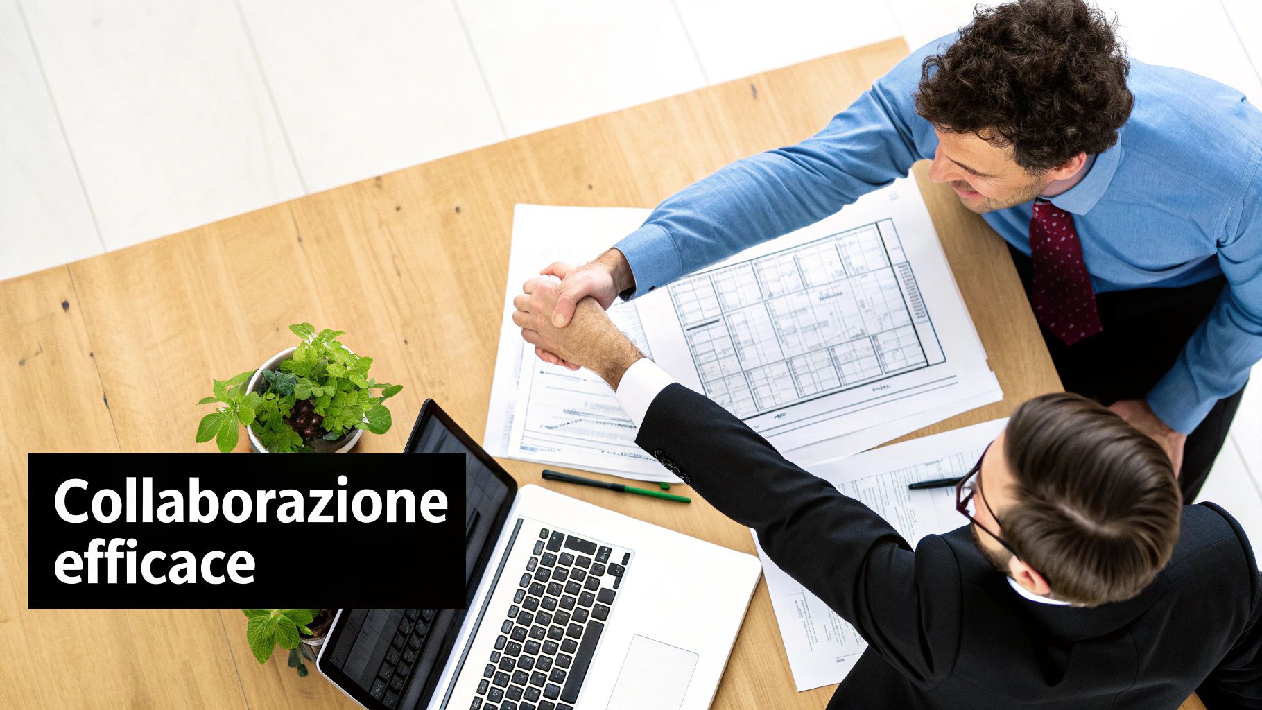 Due uomini d'affari si stringono la mano su un tavolo di legno, con laptop e documenti, simboleggiando una collaborazione efficace.