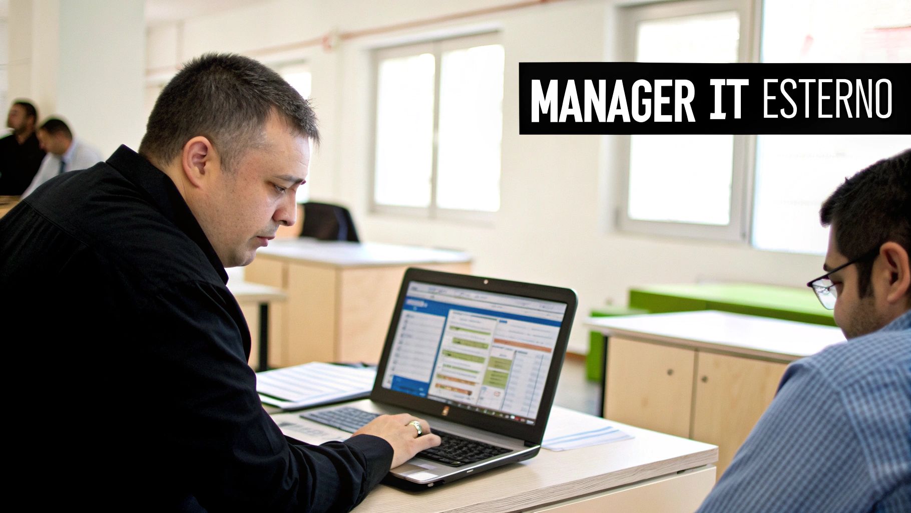 Un uomo è concentrato sul suo laptop, lavorando in un ufficio moderno, con testo "MANAGER IT ESTERNO".