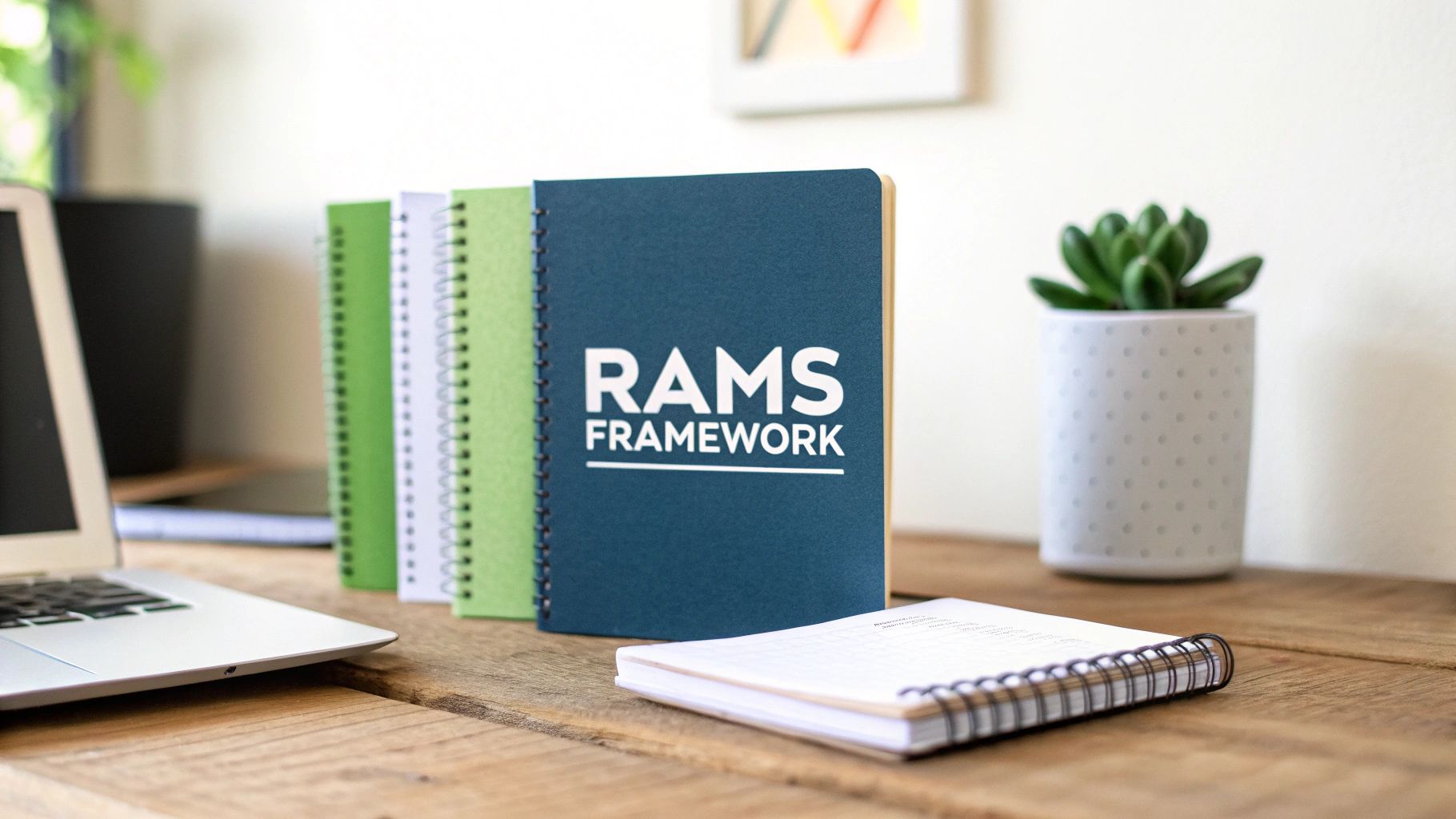 A wooden desk with a laptop, spiral notebooks, one featuring 'RAMS FRAMEWORK' logo, and a succulent.