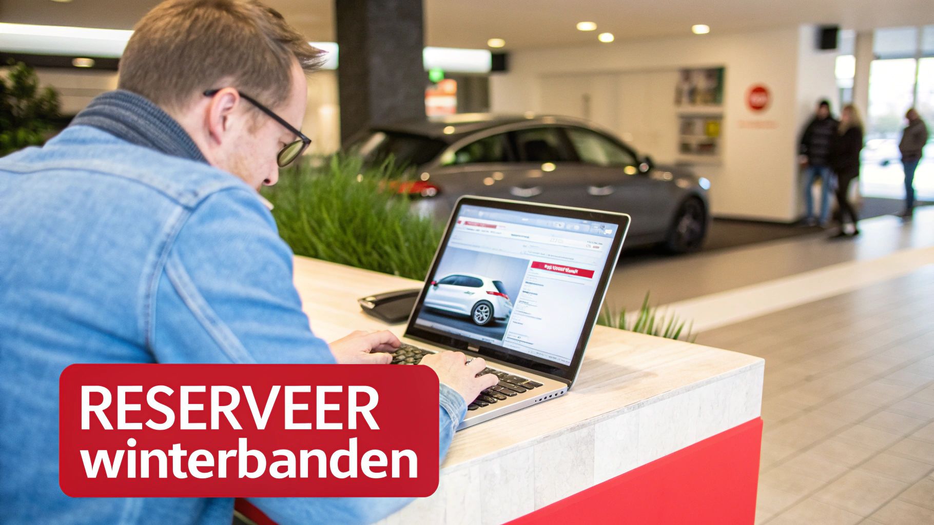 Man reserveert winterbanden online via laptop in autogarage of showroom, met auto's op de achtergrond.