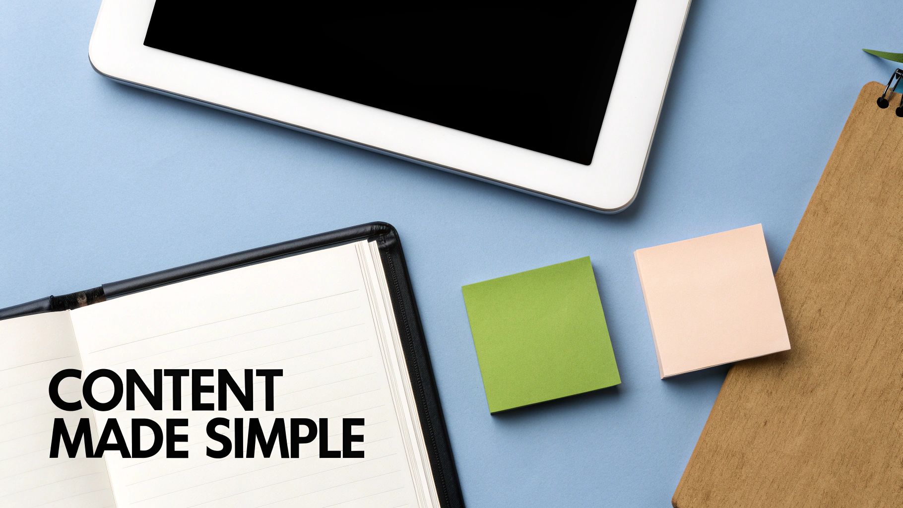 Flat lay of a workspace with a tablet, open notebook showing 'CONTENT MADE SIMPLE', and sticky notes on a blue surface.