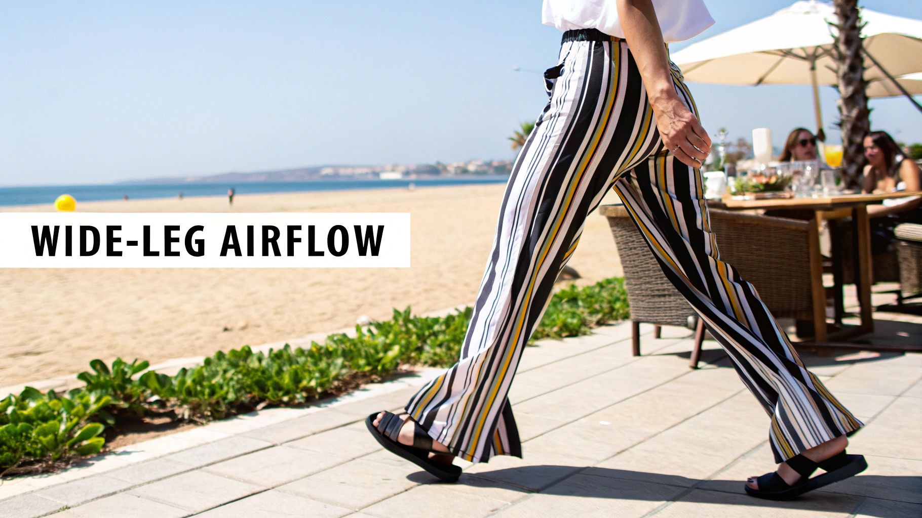 Person walking in stylish wide-leg striped pants on a sunny beach promenade.