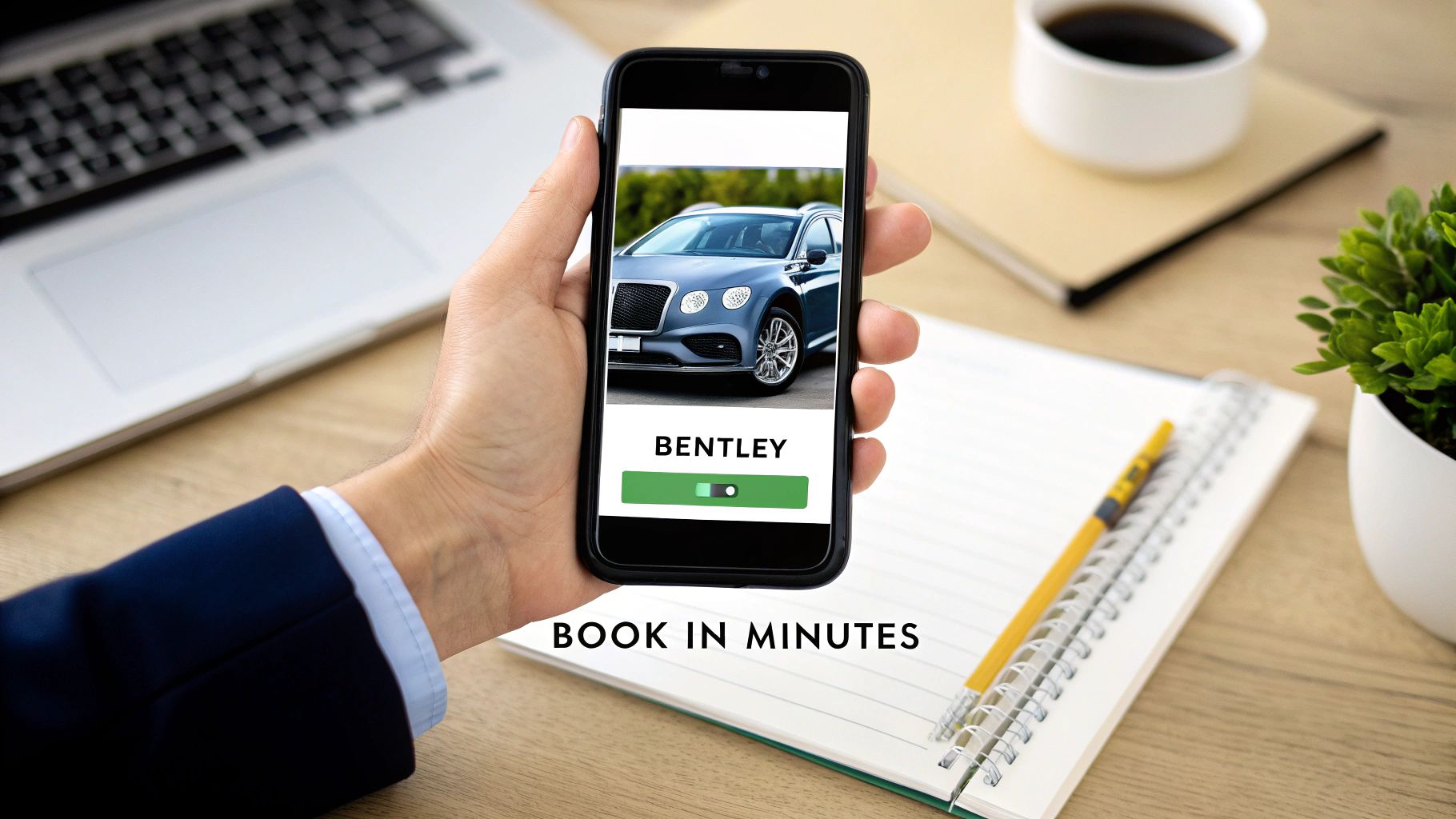 Rent a Bentley in Dubai a Guide to Ultimate Luxury 2 A hand holds a smartphone displaying a Bentley car booking app on a wooden desk with a laptop.