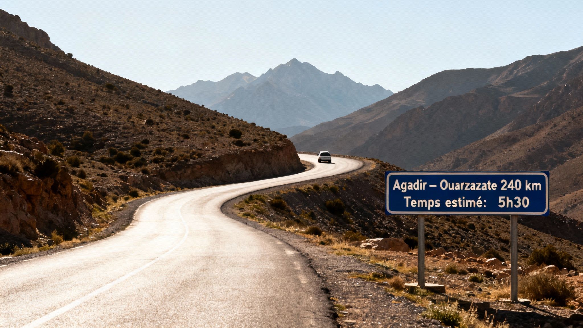 Route sinueuse en montagne avec un panneau indiquant Agadir-Ouarzazate (240 km, 5h30) et une voiture au loin.