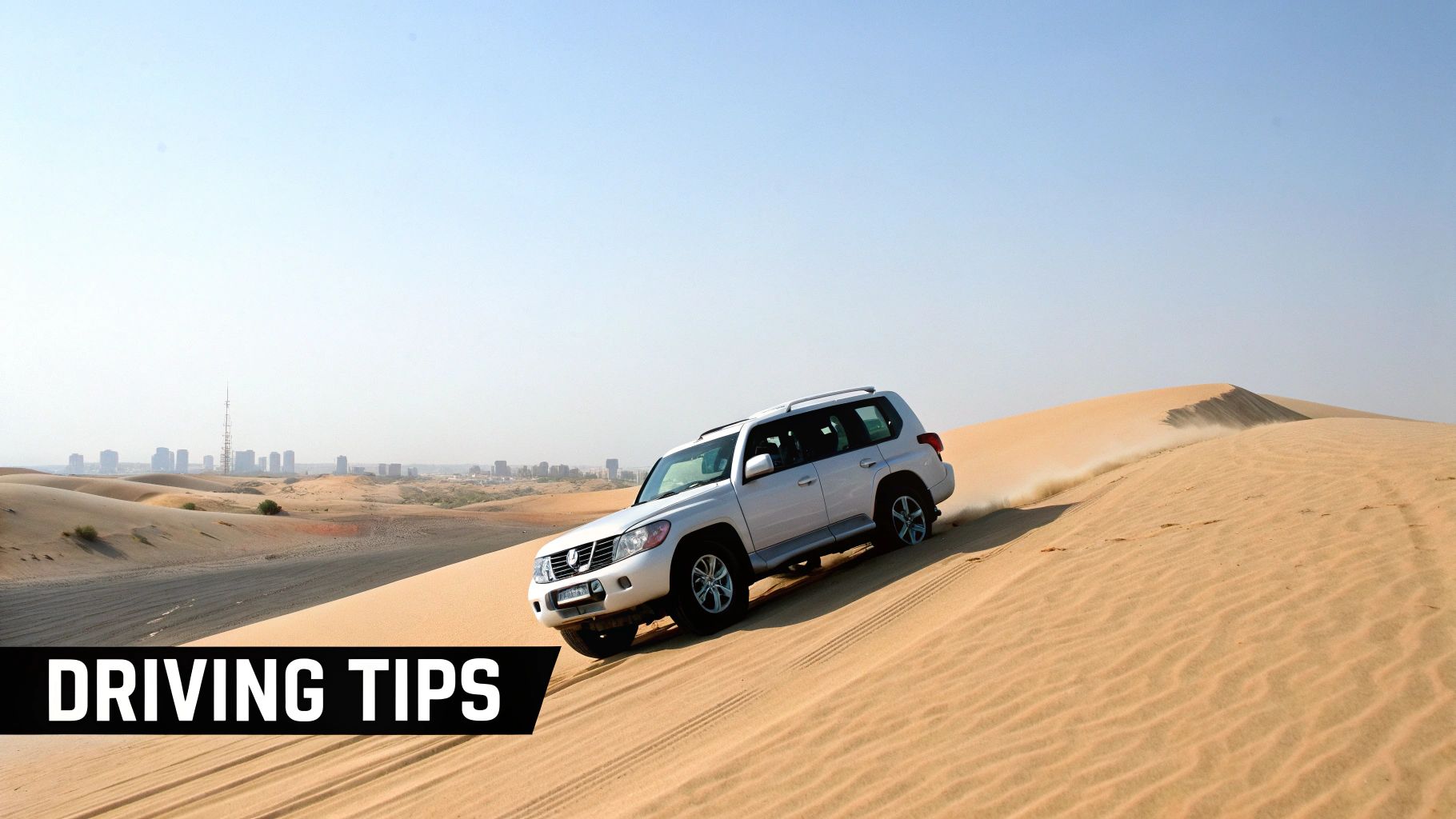 A white SUV off-roading on sand dunes, kicking up sand, with a city skyline in the background.